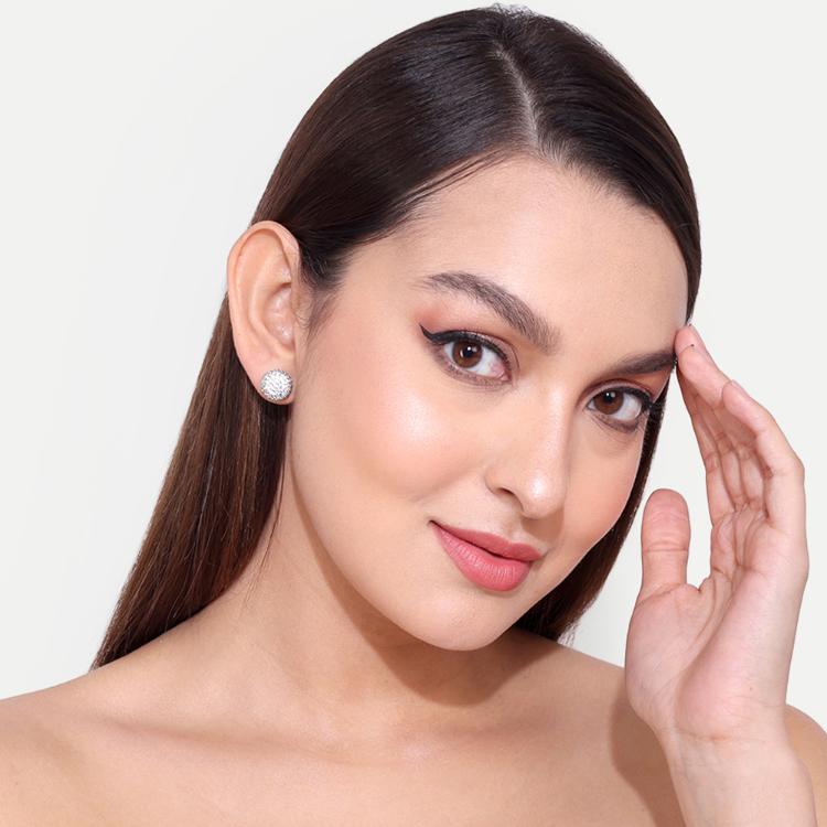 Close-up of woman wearing round stud earrings with sparkling details against a background