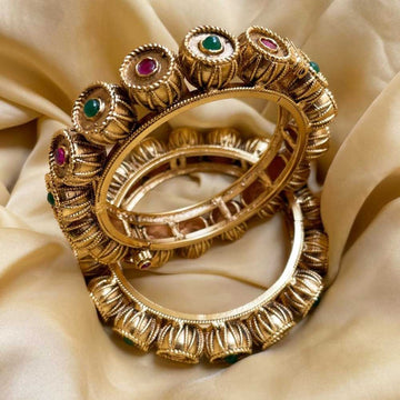 Close-up of ornate gold Festive Bangles with red and green stones on silky fabric background