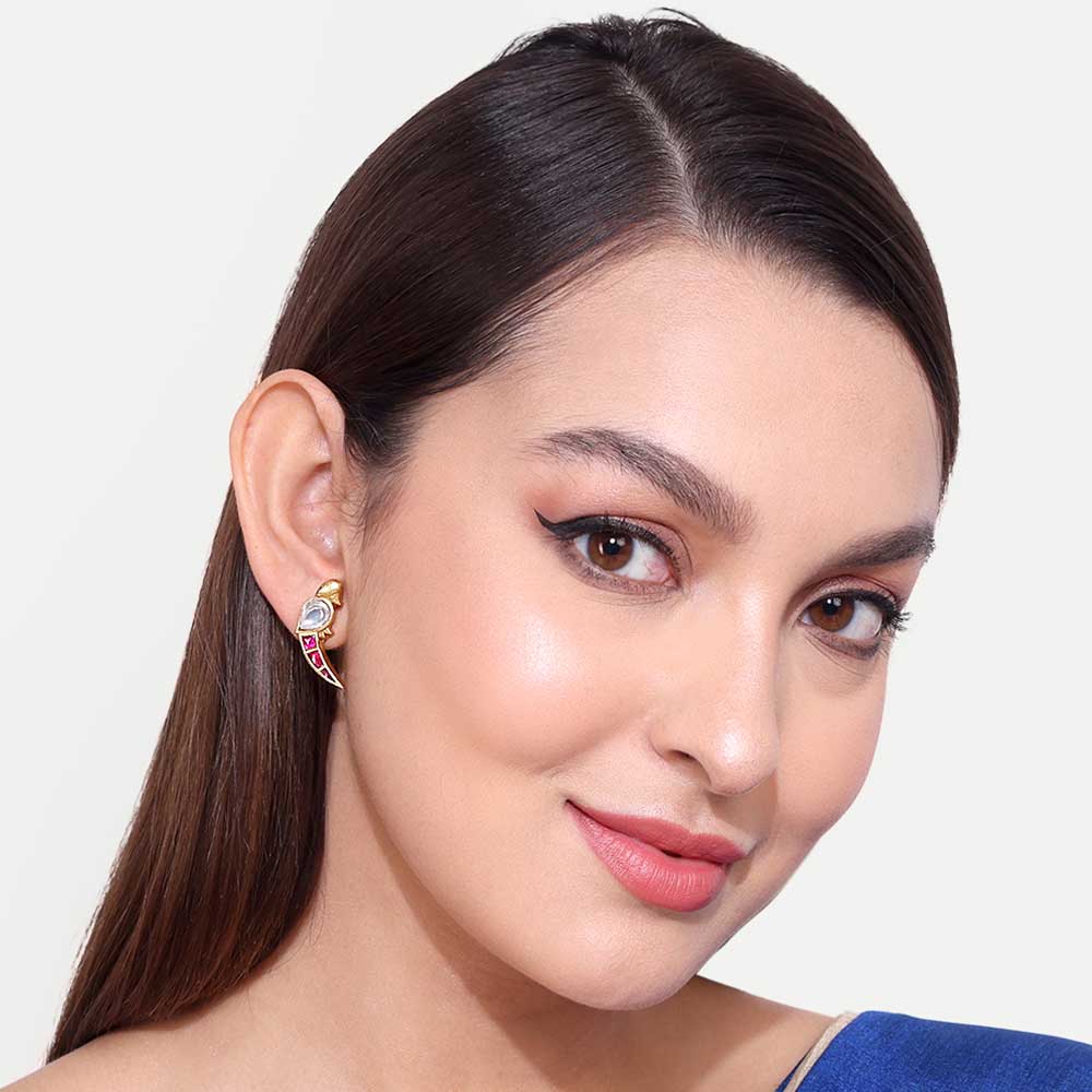 Woman wearing a stylish gold earring with colorful detailing against a white background