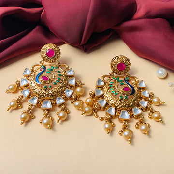 Pair of ornate antique earring with gold finish, green and pink enamel detailing and pearl dangles on beige background