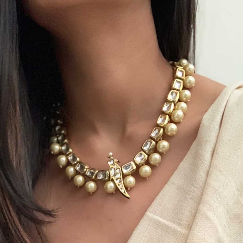 Elegant Kundan Necklaces featuring gold settings and pearl accents worn on neck with beige attire