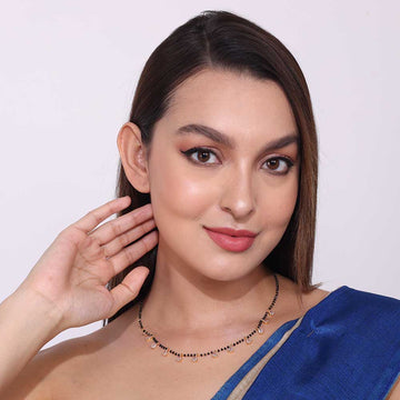 Woman wearing a delicate short mangalsutra necklace with black and gold beads and small hanging charms