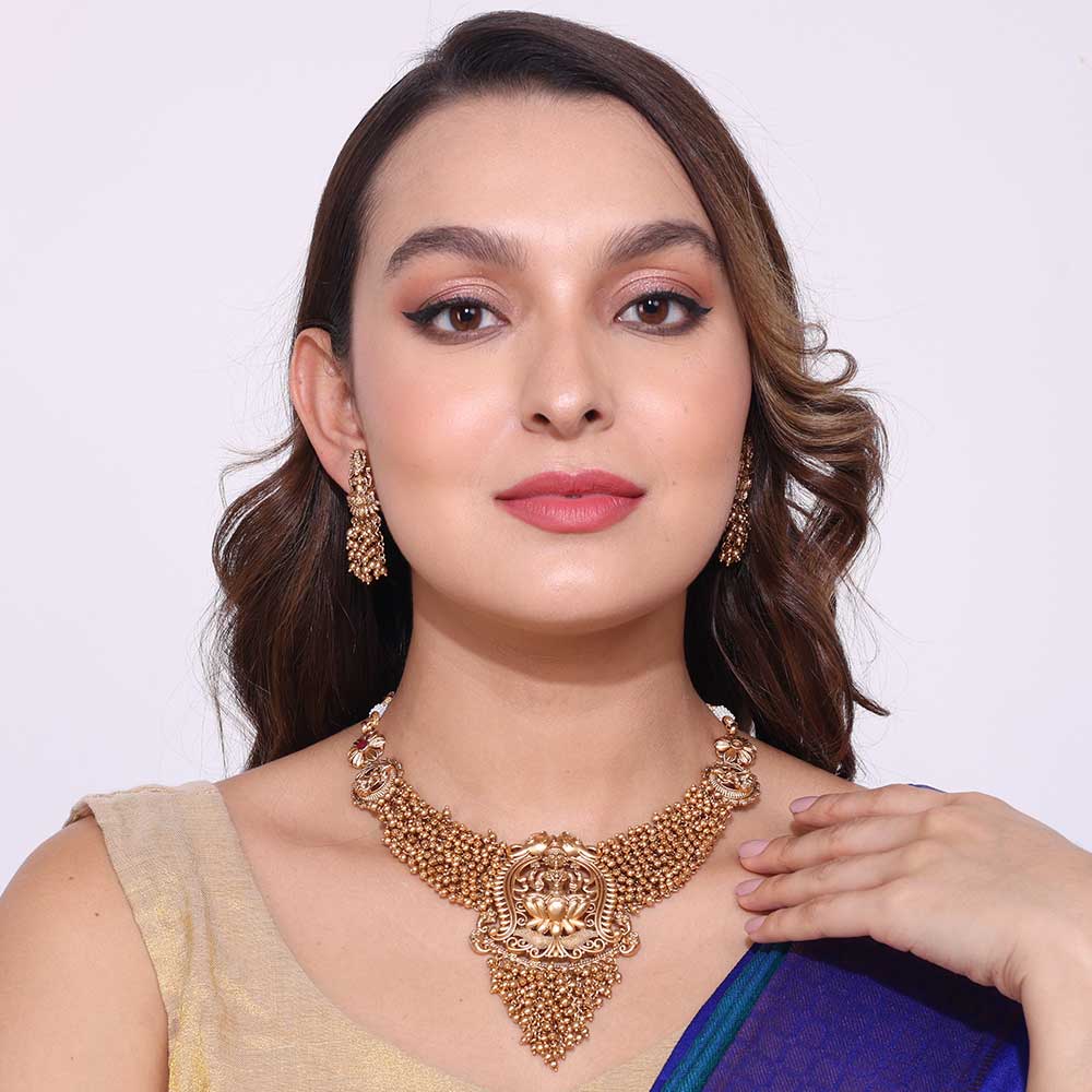 Woman wearing traditional gold temple necklaces and matching earrings with a beige and blue outfit