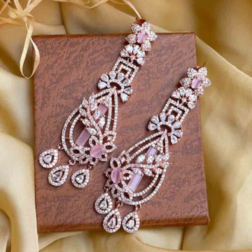 Elegant pair of rose gold earring with intricate design and pink gemstone accents displayed on a textured box