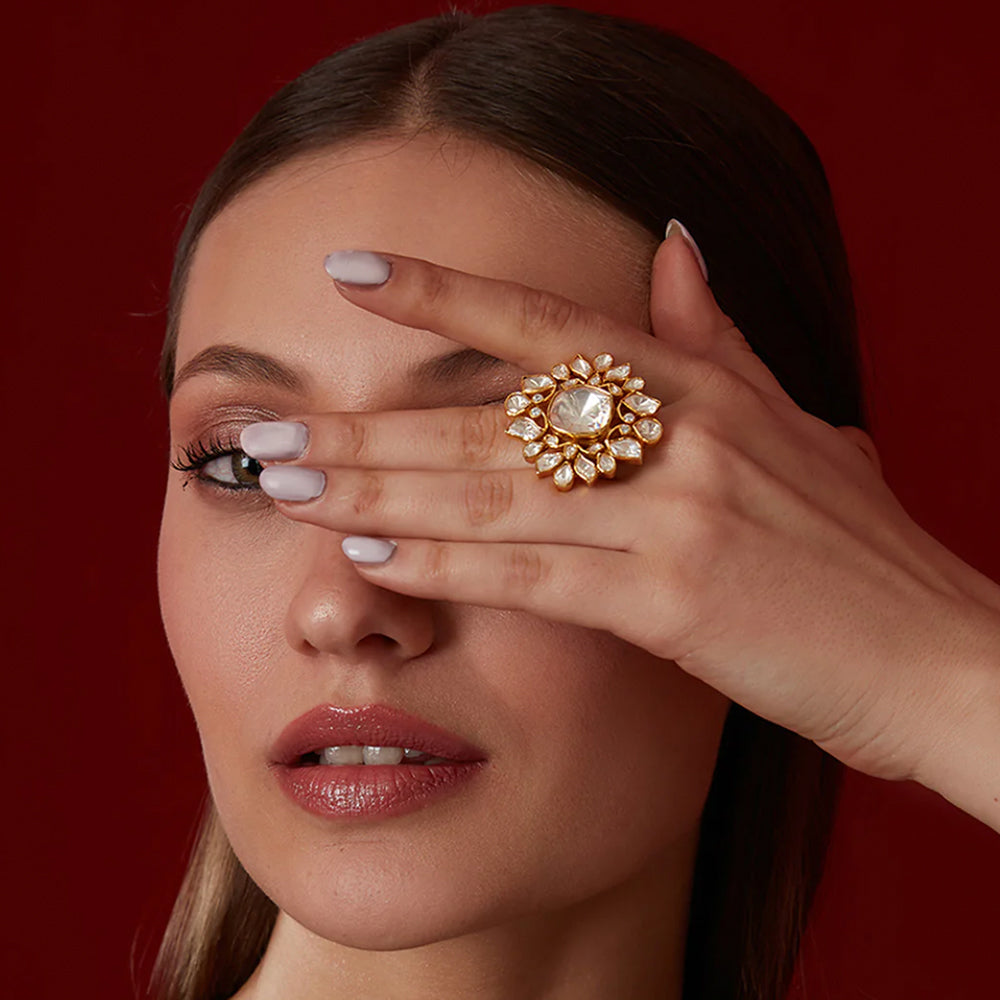 Close-up of a woman wearing a large ornate finger ring wedding covering one eye against a red background