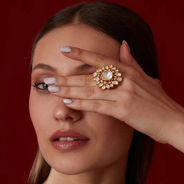 Close-up of a woman wearing a large ornate finger ring wedding covering one eye against a red background
