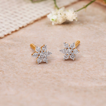 Elegant flower-shaped daily wear diamond studs with gold posts laid on a beige surface