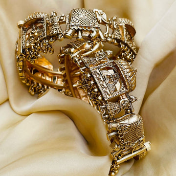 Intricately designed gold-tone bridal bangles with traditional motifs on soft beige fabric