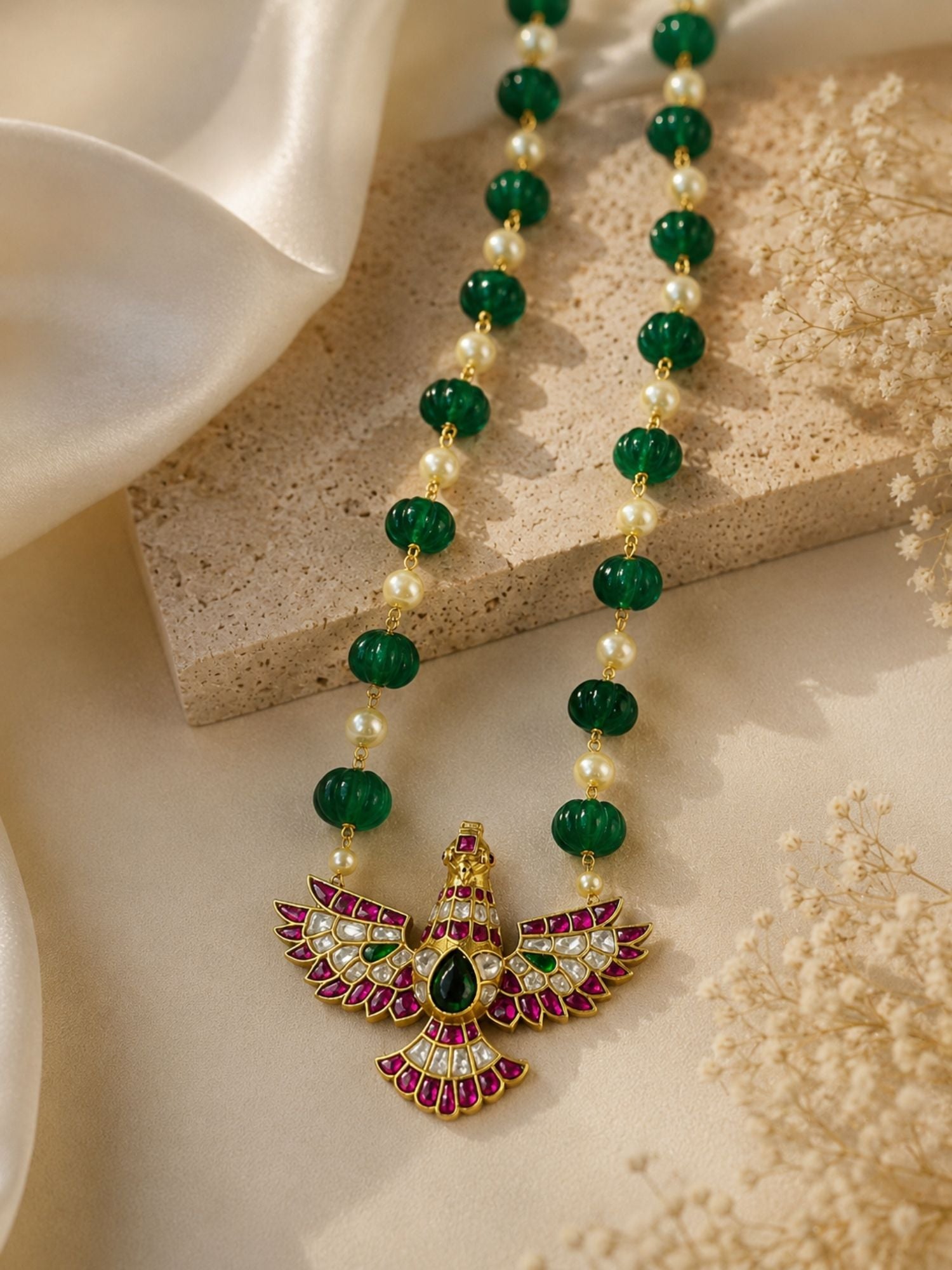 Gold plated green bead and pearl Kundan necklace with bird pendant, styled flat lay with dried flowers