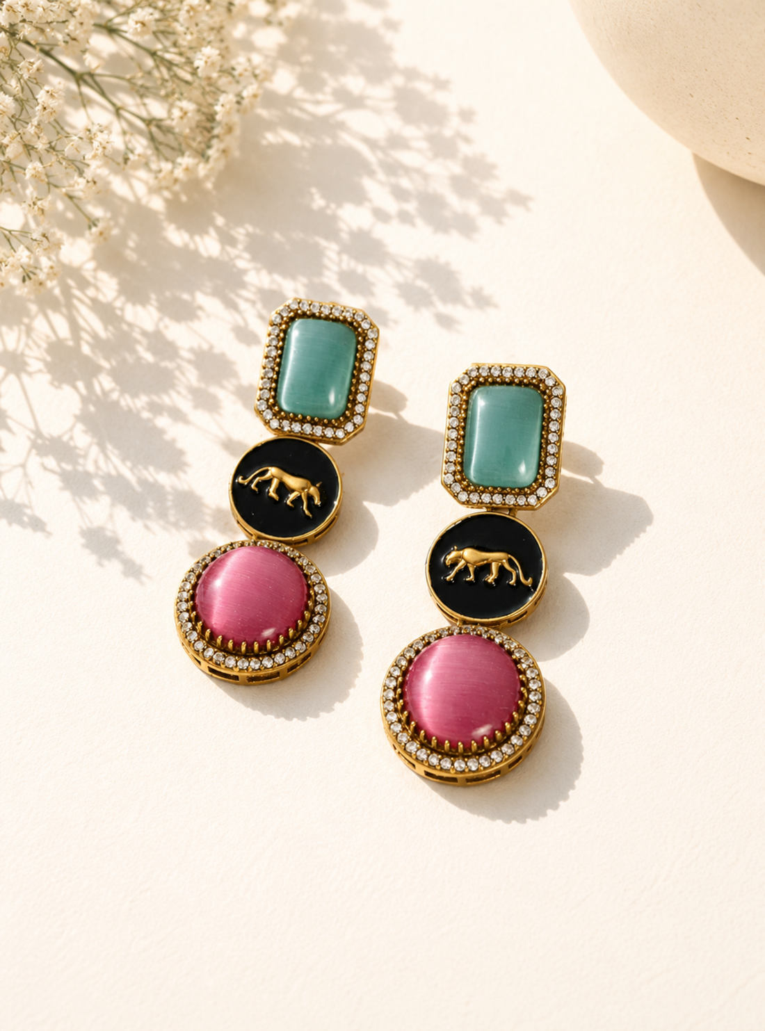 Colorful earrings with pink, green, and black stones on a light background