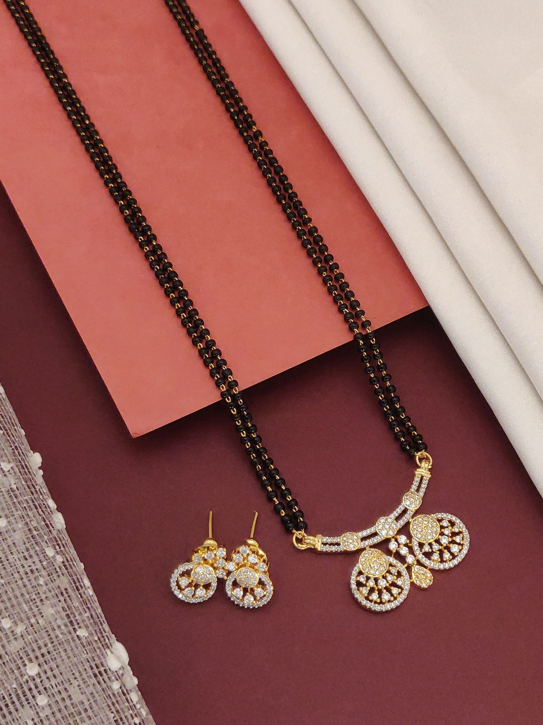 Abdesigns Black Beads CZ Pendant Mangalsutra With Earrings gold CZ pendant and matching round earrings on maroon background