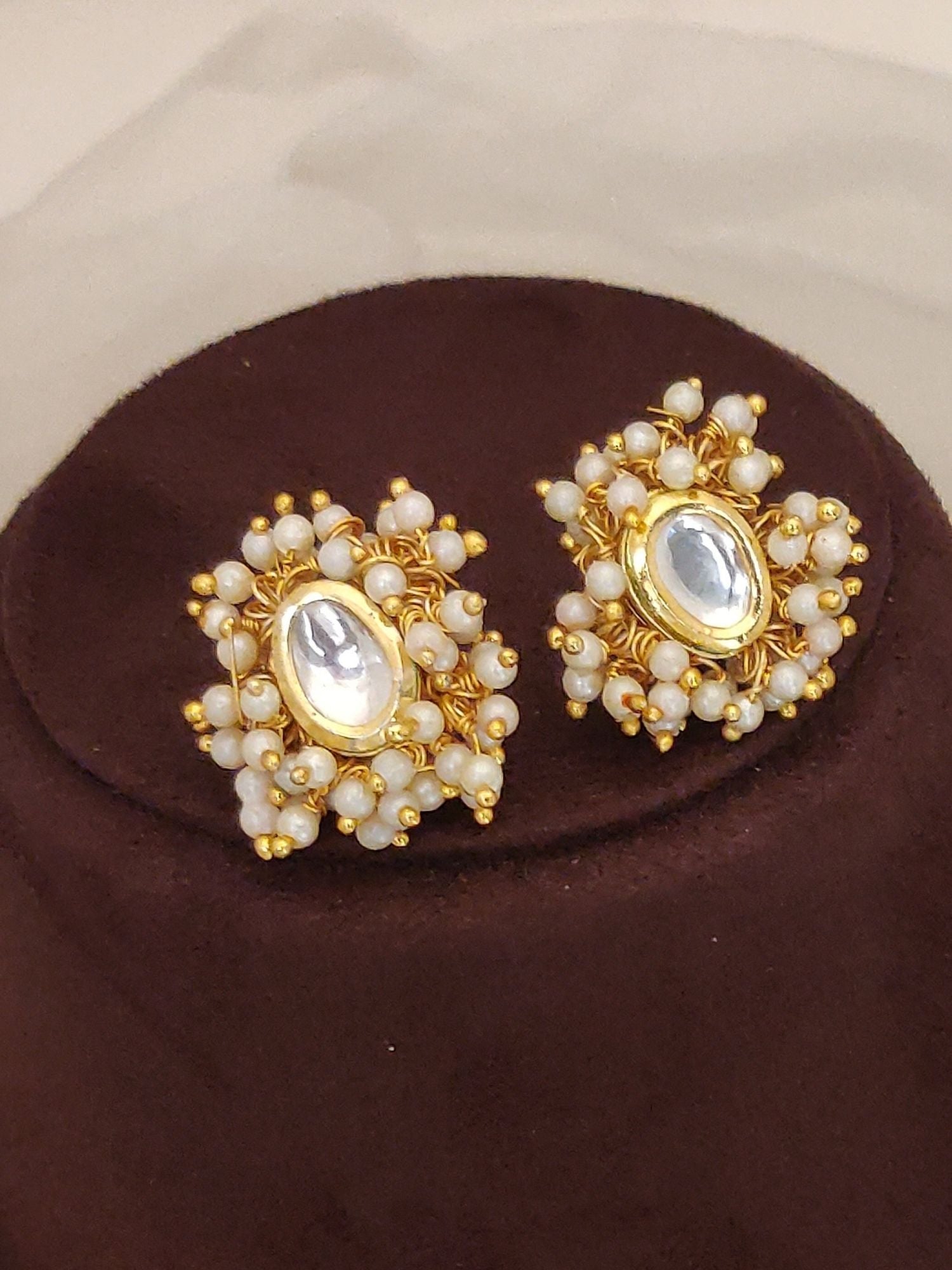Abdesigns Bridal White Kundan Pearl Choker Set displayed as gold kundan and white pearl earrings on a brown cushion