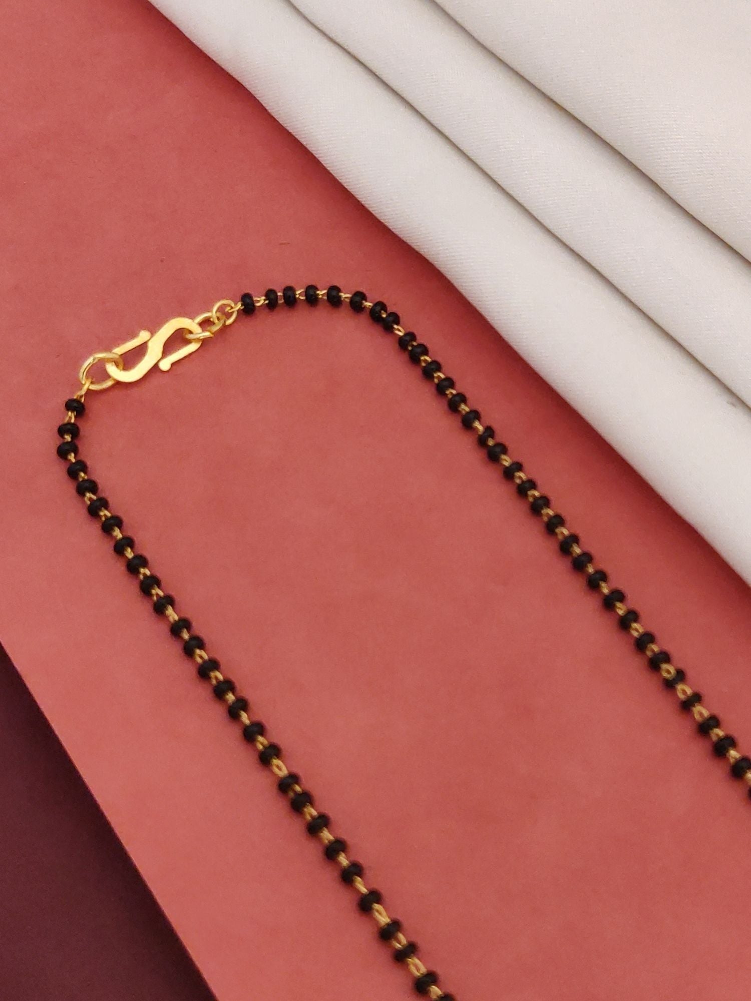 Abdesigns Gold-Plated CZ Mangalsutra with Earrings.. black beaded chain with gold clasp displayed on red background