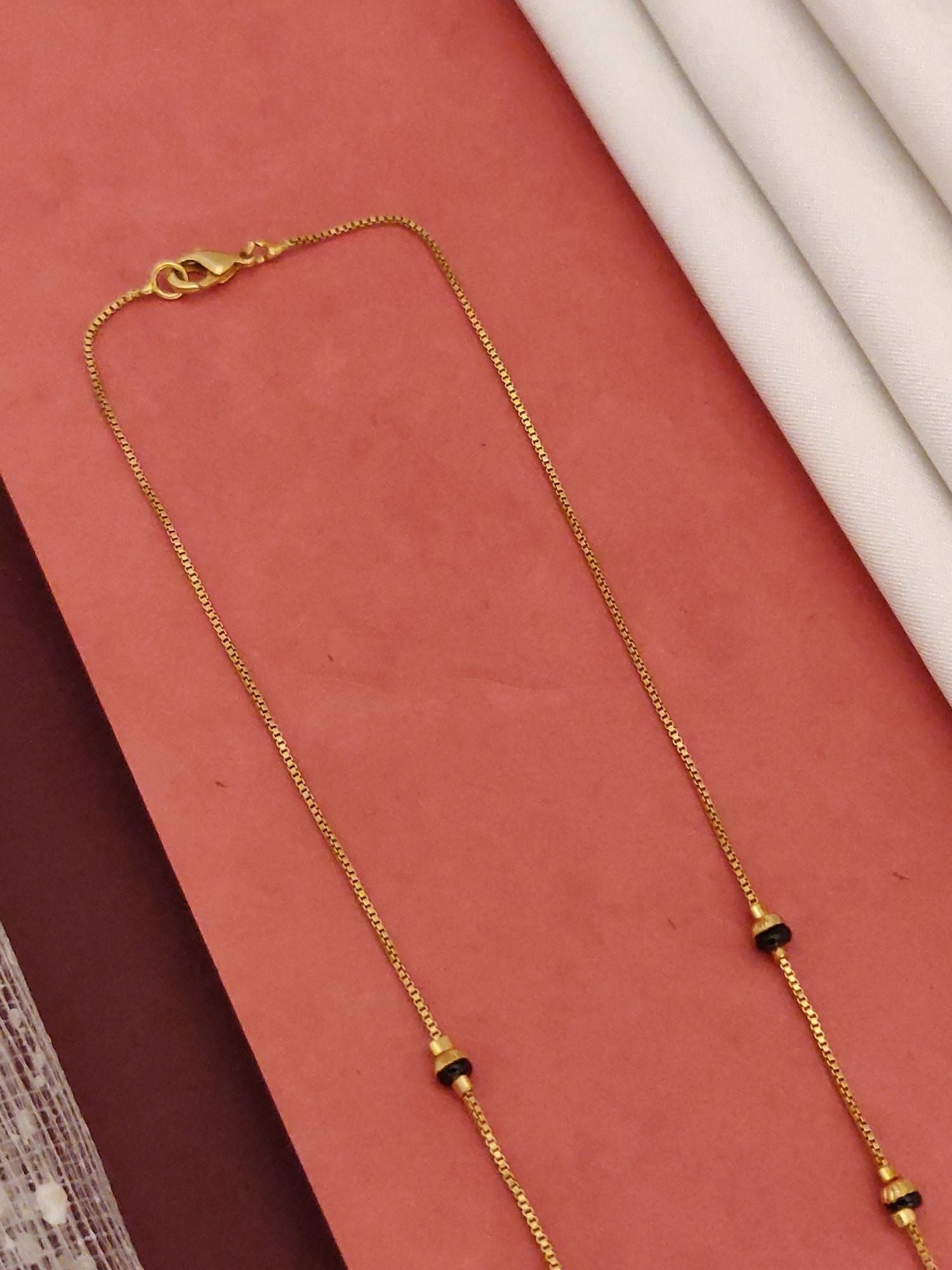 Abdesigns Gold-Plated Mangalsutra with CZ Drops thin gold chain with black beads on pink background