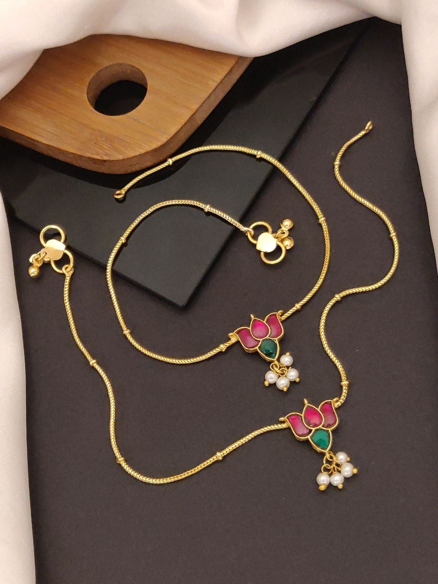 Abdesigns Jewellery Gold Anklets with Lotus Pendants shown as two gold enamel lotus anklets with pearl drops on dark backdrop