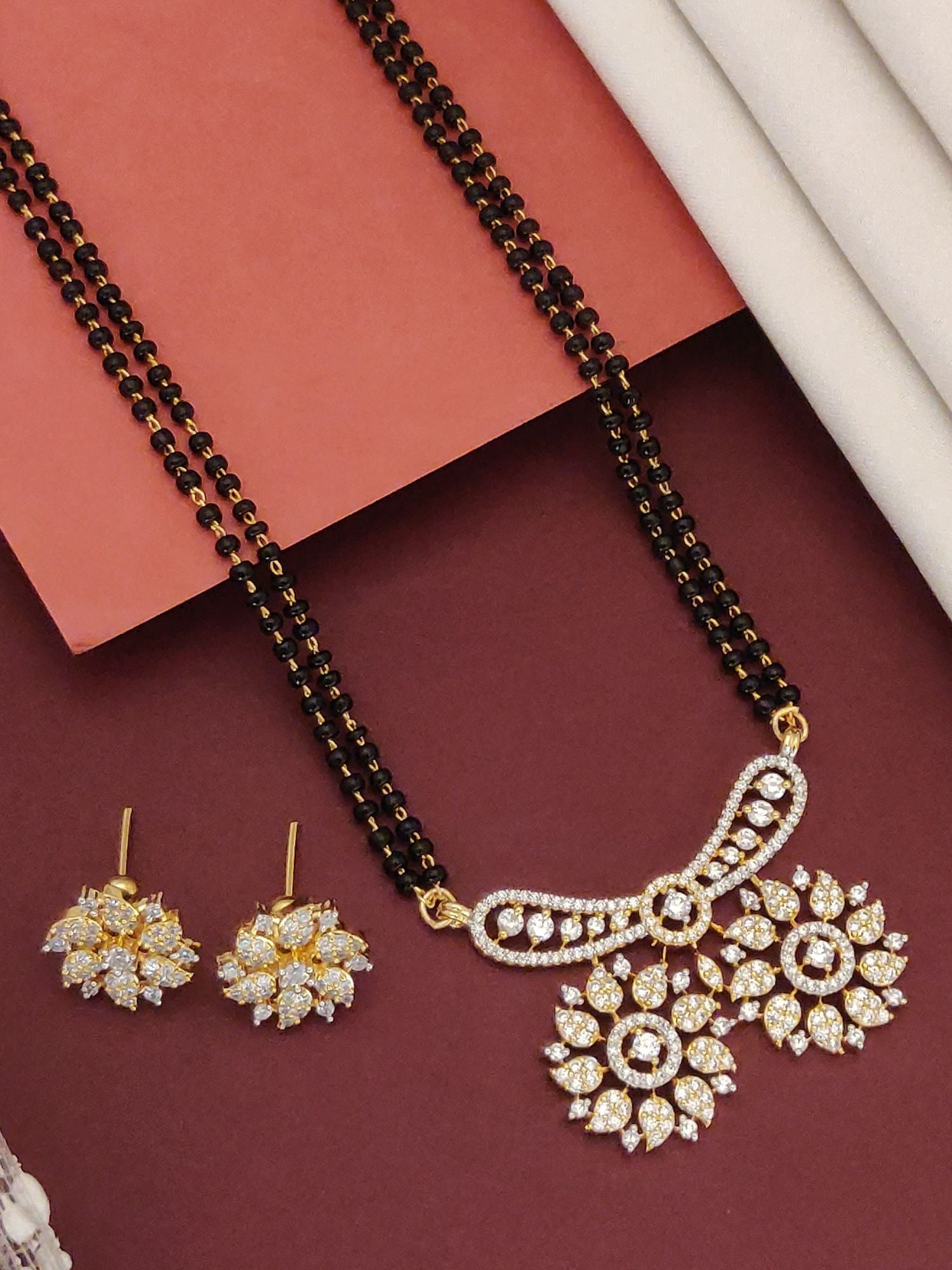 Abdesigns Mesmerizing gold plated mangalsutra for women. Double black bead chain with floral CZ pendant and matching earrings