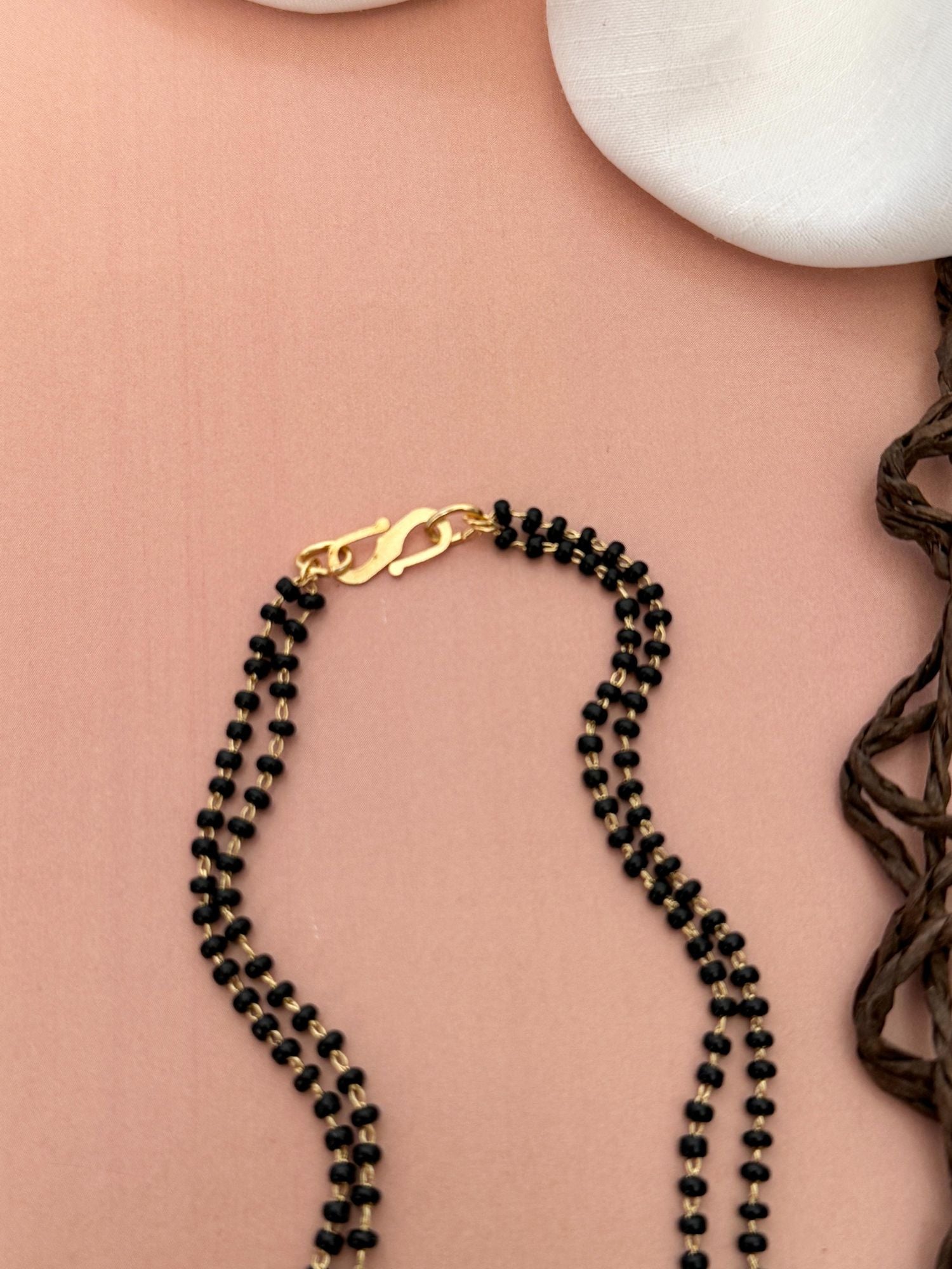 Abdesigns Opulent gold plated mangalsutra for women. Double strand black beads with gold clasp on peach background