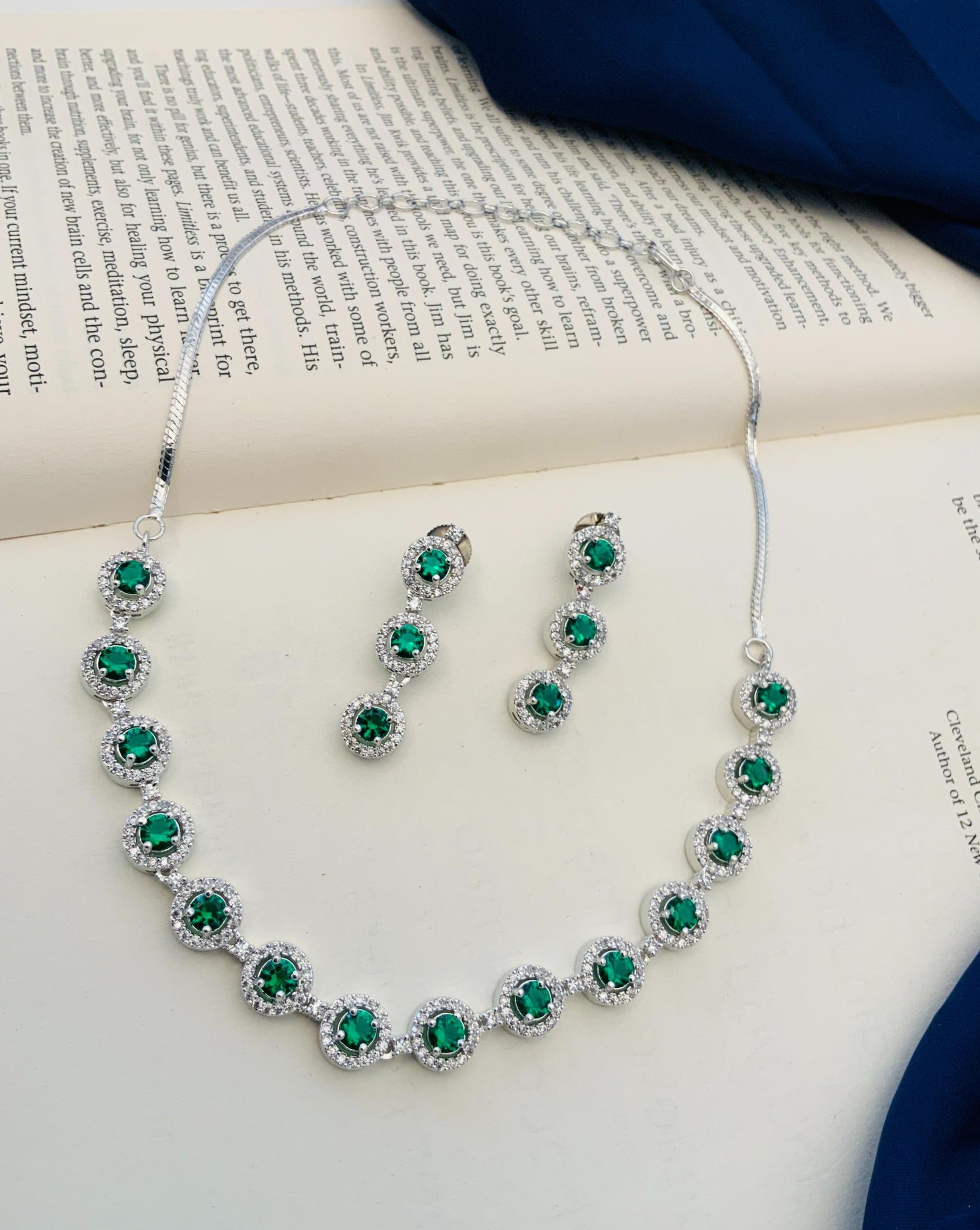 Abdesigns Silver Plated American Diamond Necklace Set featuring green stones and matching drop earrings displayed on book