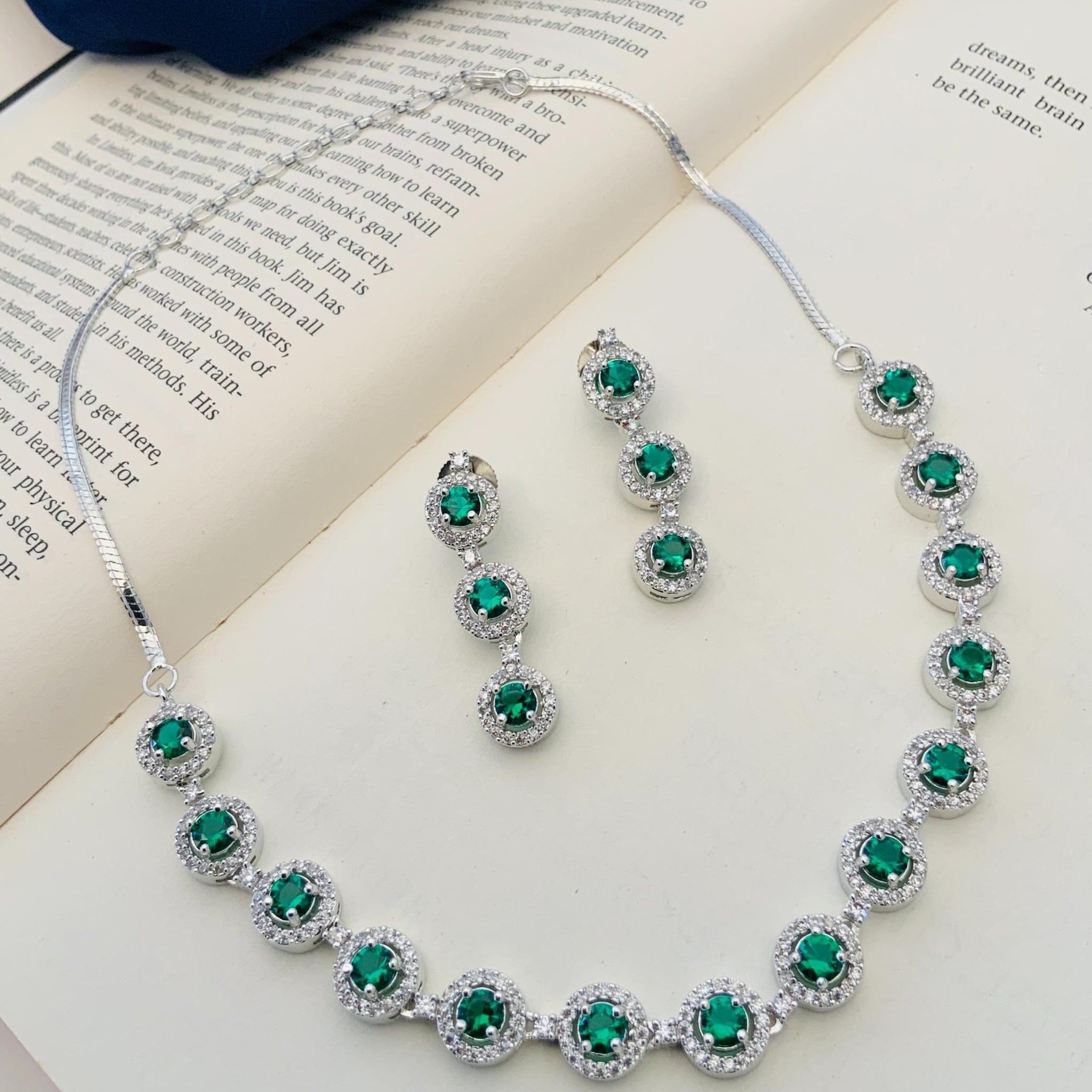 Abdesigns Silver Plated American Diamond Necklace Set with green emerald stones and matching earrings on open book