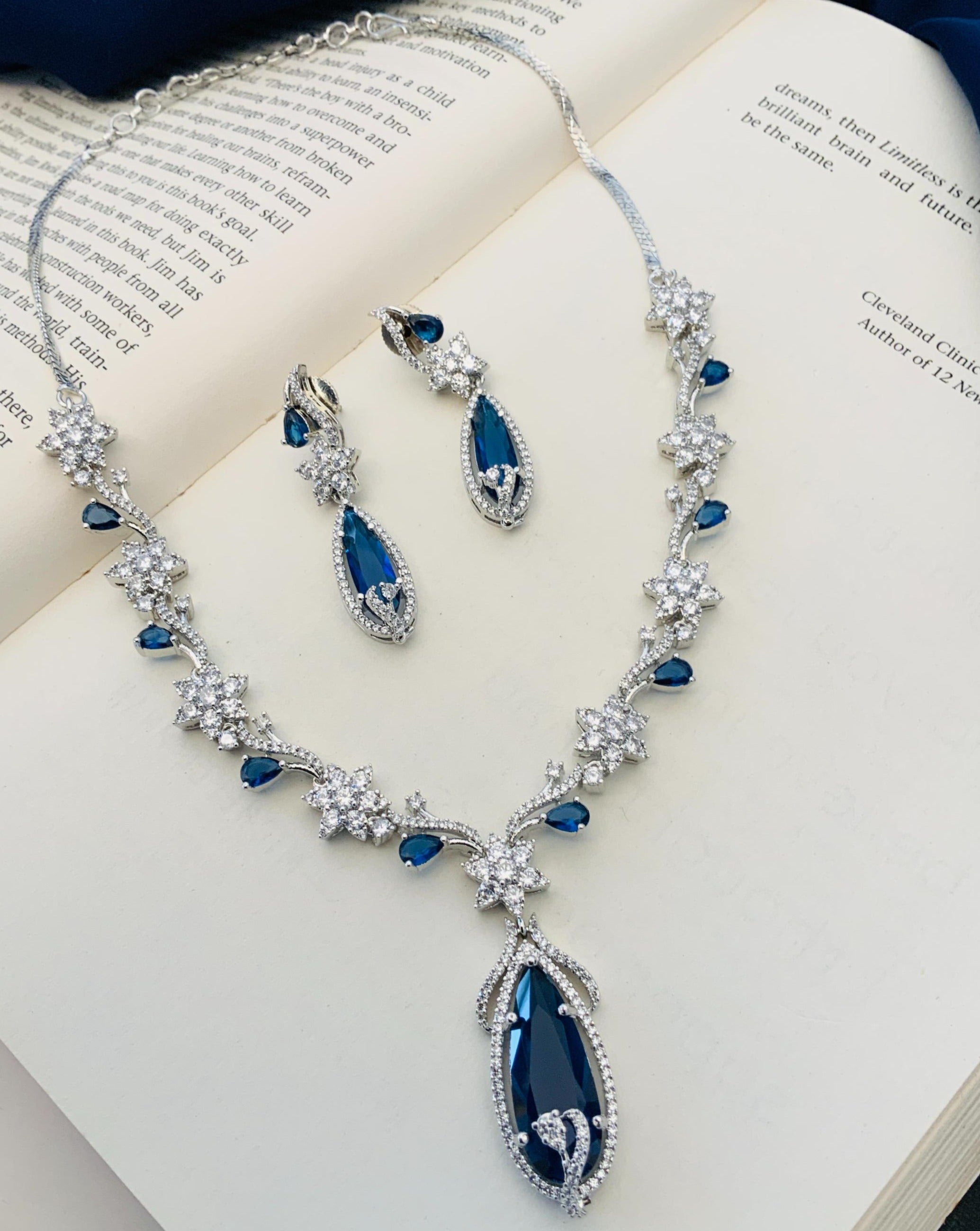 Blue Sapphire Silver Plated American Diamond Necklace Set with matching earrings on open book