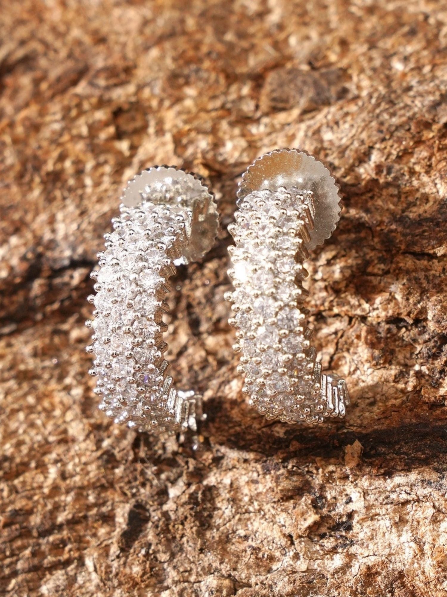 Delicate Silver Plated American Diamond Earring pair with sparkling stones on textured brown background
