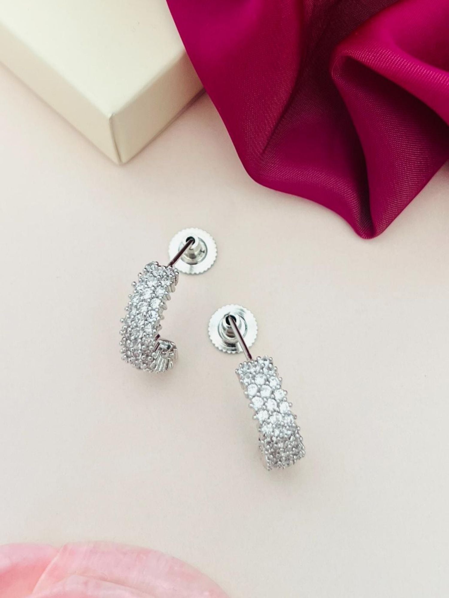 Delicate Silver Plated American Diamond Earring from Abdesignsjewellery displayed on a soft beige surface with pink and red fabric