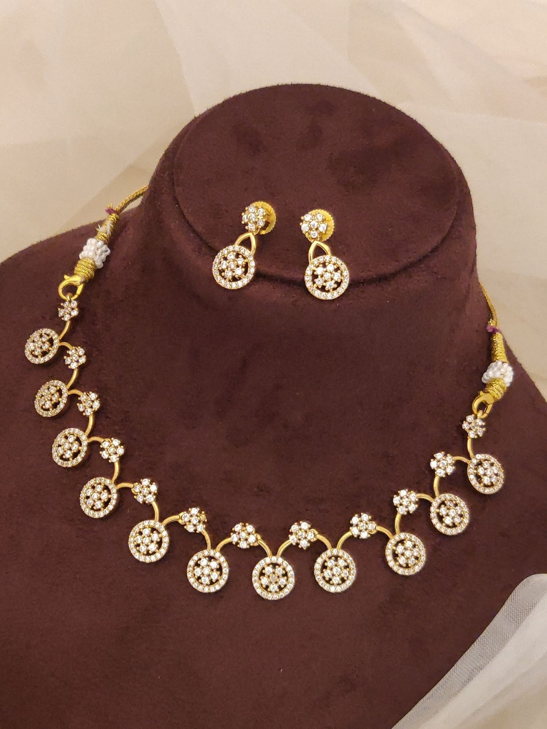 Designer gold plated fashion jewelry india gold necklace with circular stone motifs and matching earrings displayed on brown bust