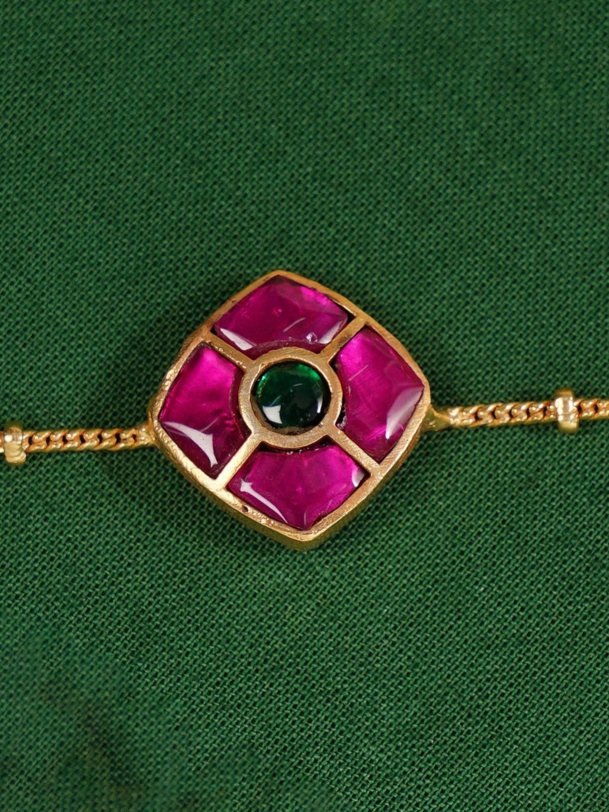 Close-up of Enchanting Gold Plated Kemp Kundan Floral Anklets with pink and green stones on a green fabric background