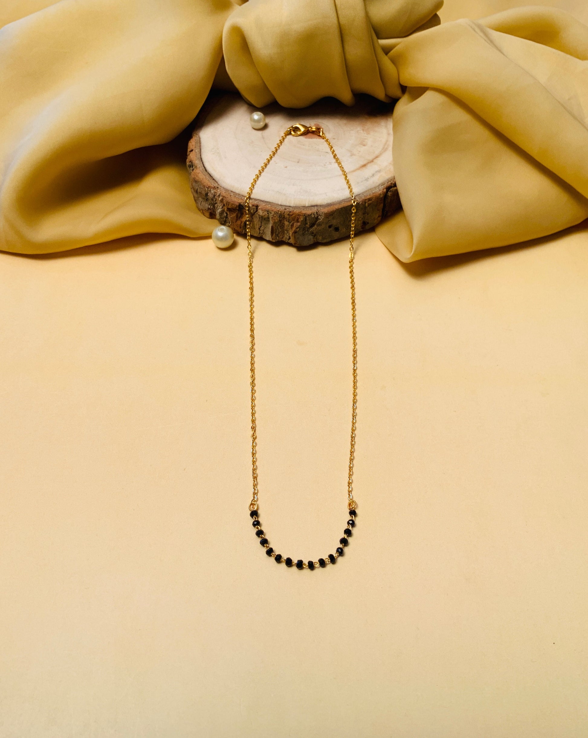 Gold Plated American Diamond Mangalsutra with black beads on a beige fabric and wooden background