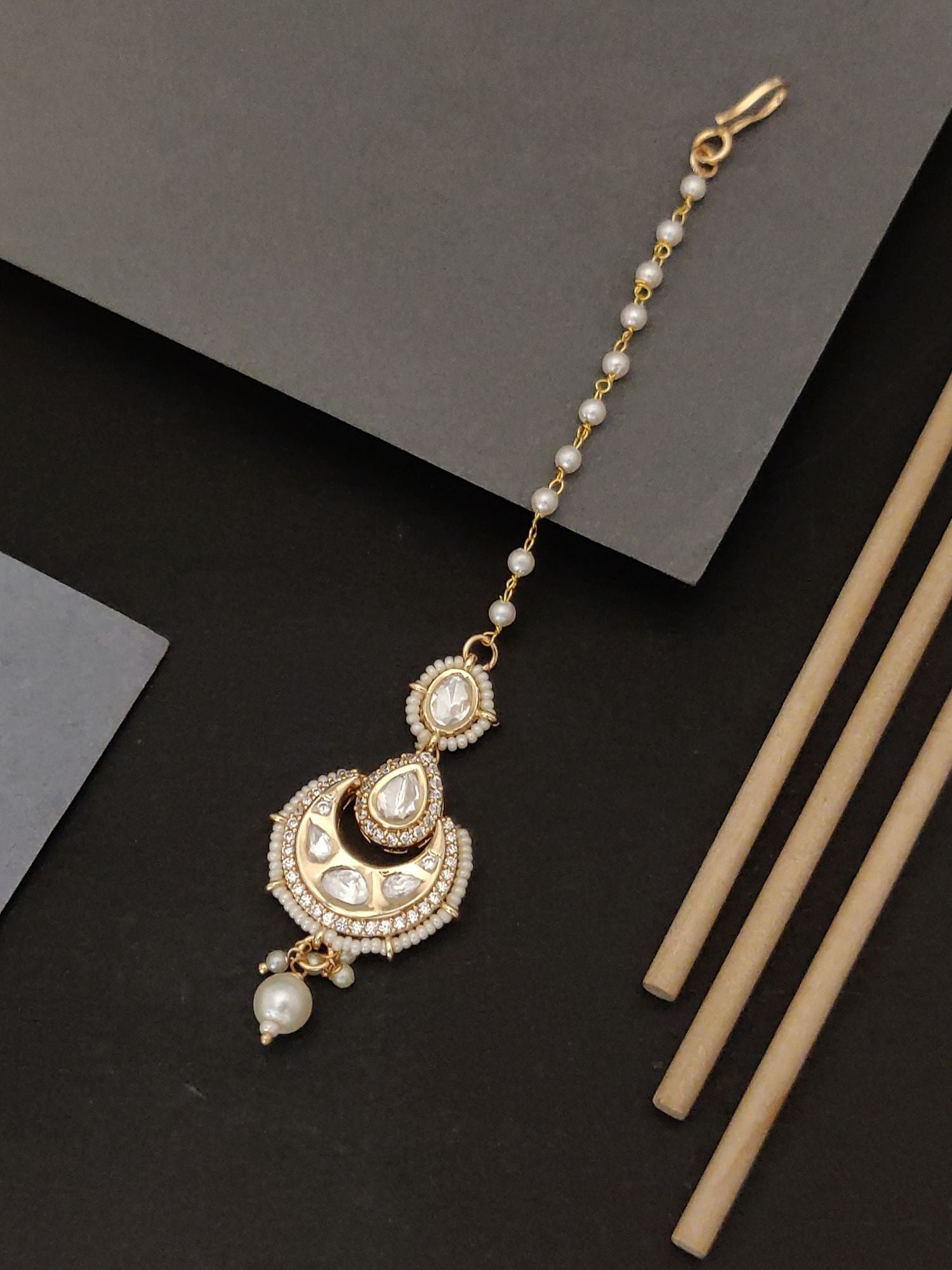 Gold plated bridal polki maangtikka with intricate pearl and stone detailing on black background