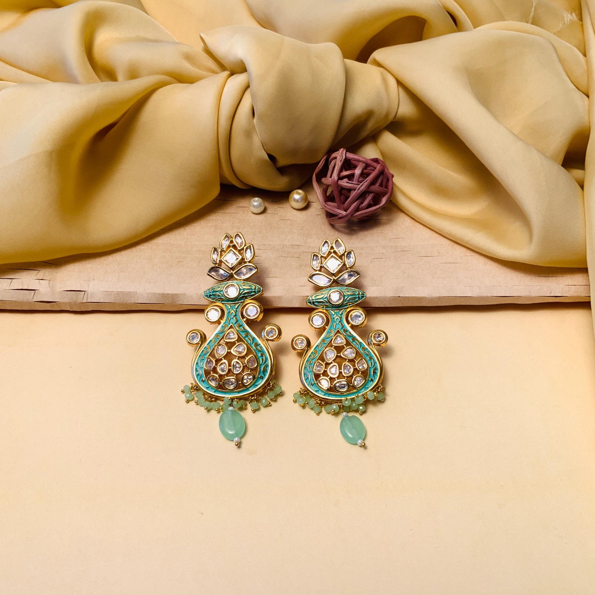 gold plated kundan meenakari earrings with green enamel and teardrop beads on satin cloth