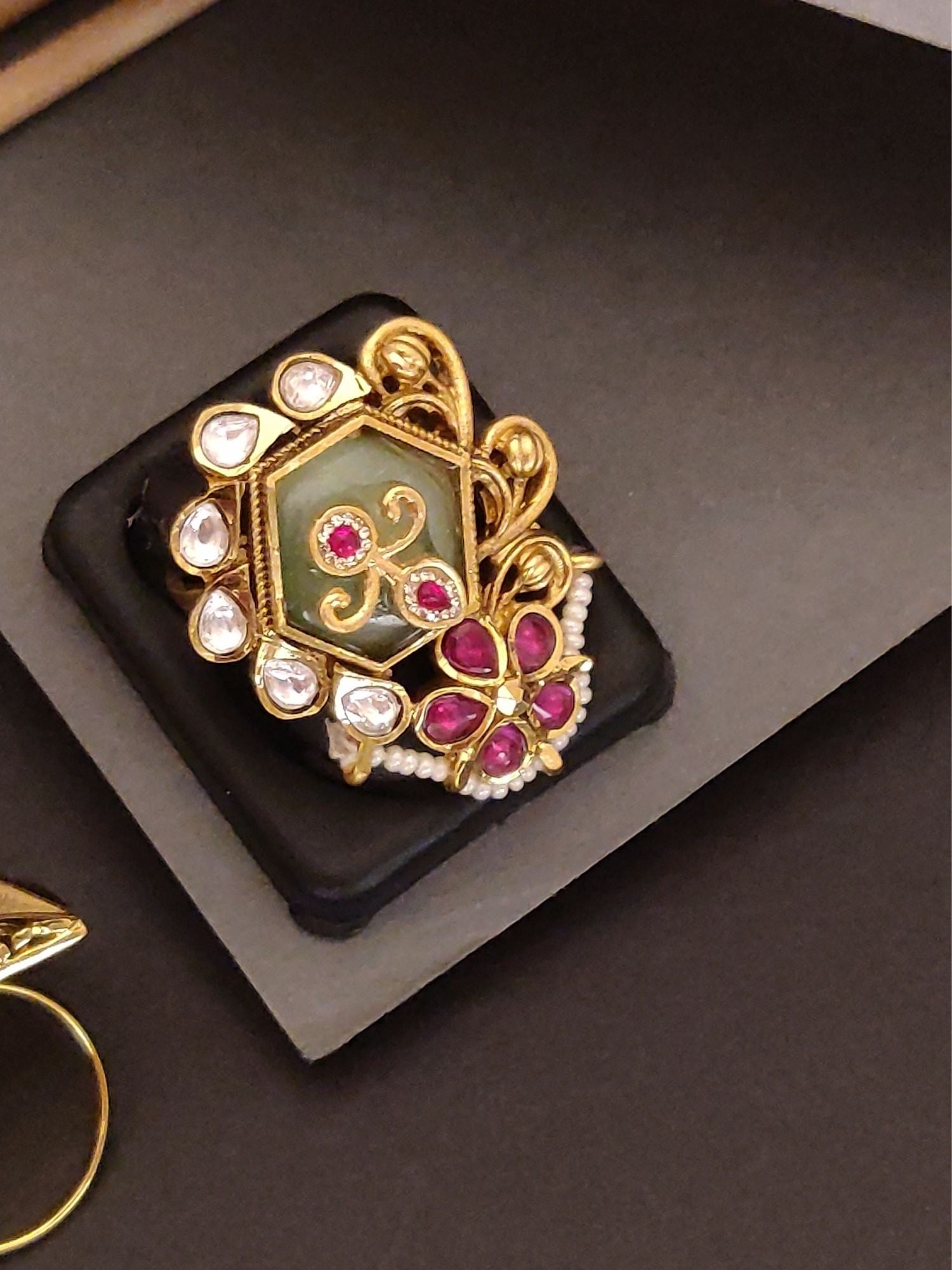 gold plated ruby kundan ring with green enamel center teardrop kundan stones pearl trim on display