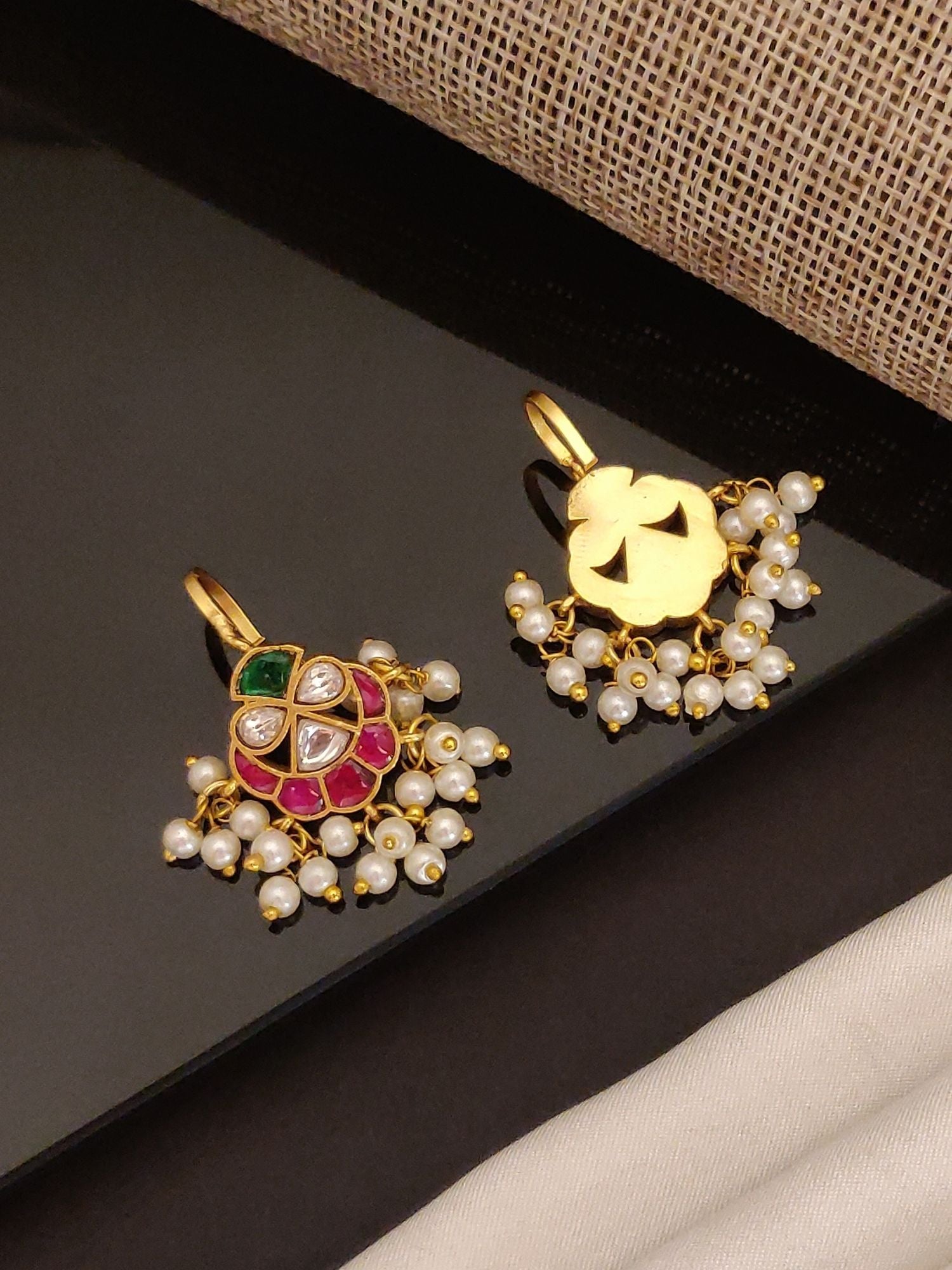 Pair of gold tone pearl stone earrings with red and green kundan accents and dangling pearl clusters on black display