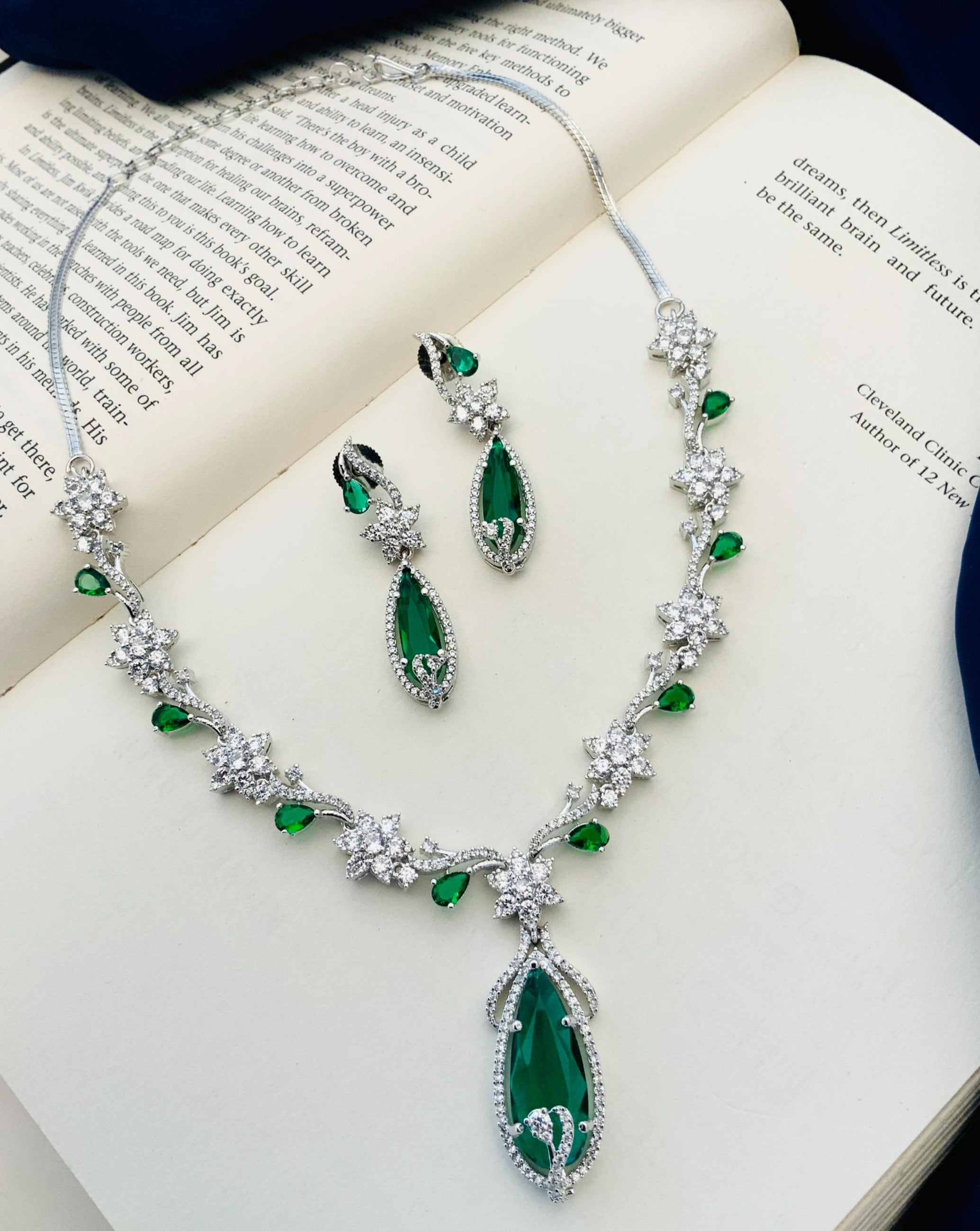 Blue Sapphire Silver Plated American Diamond Necklace Set with green stones and matching earrings on an open book