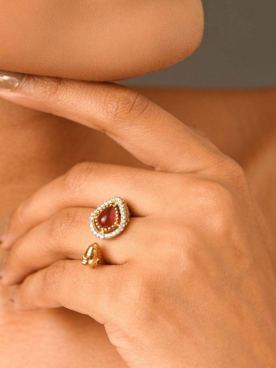 Model wearing peacock gold plated kundan ring teardrop red stone with pearl halo on finger near face