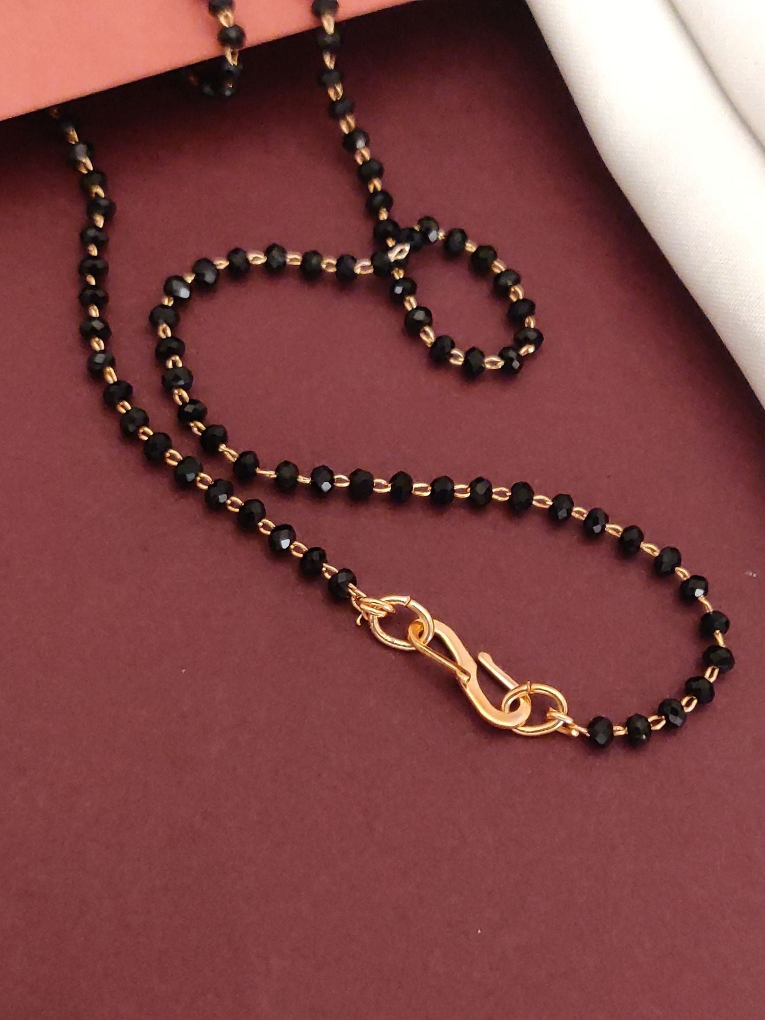 Abdesignsjewellery rose gold plated mangalsutra for women with black beads and rose gold clasp on burgundy background