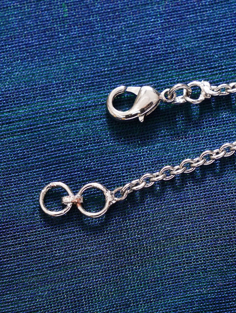 Close-up of Round Shape AD Silver Plated Watch Charm chain clasp on blue fabric background