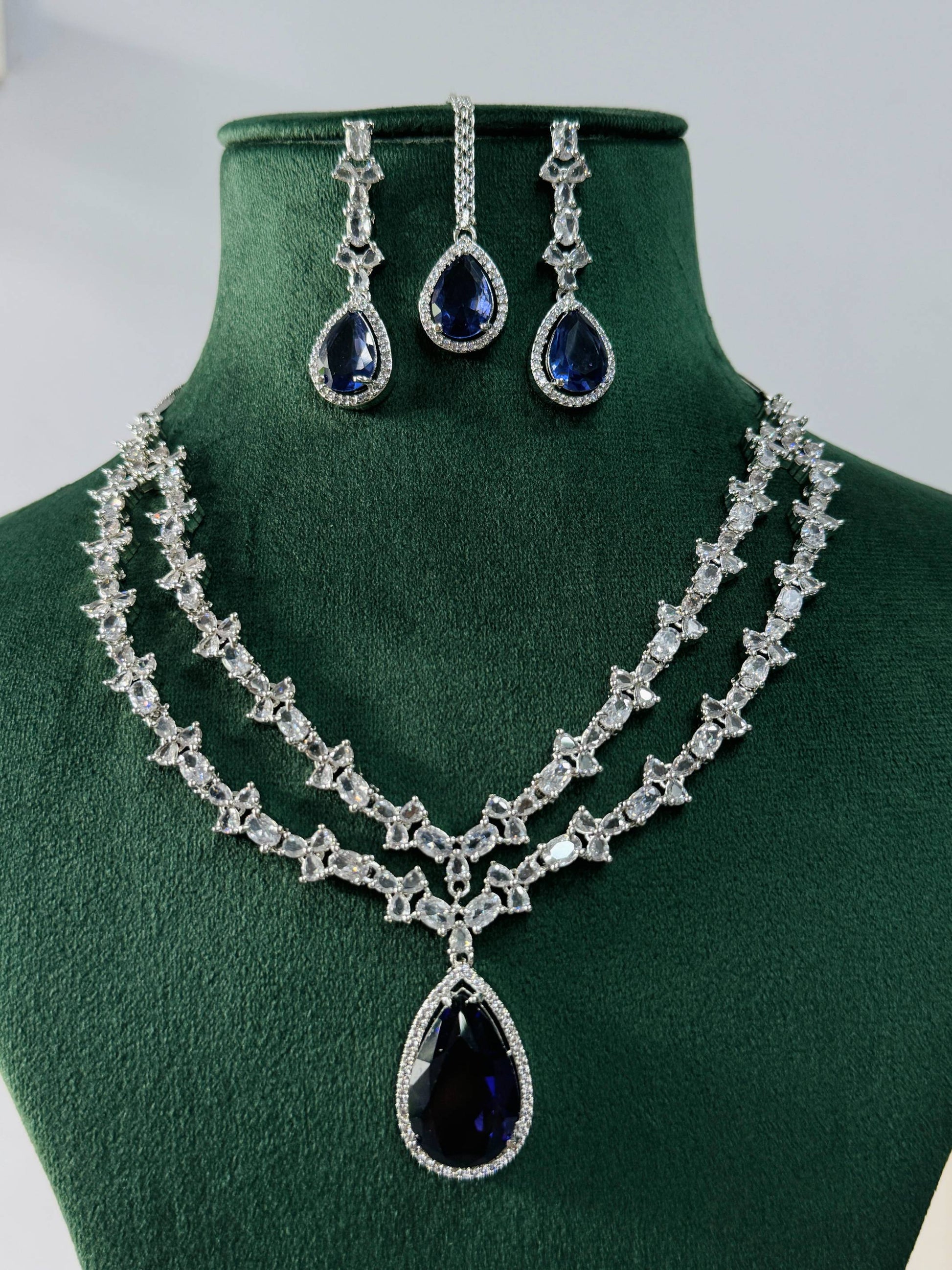 Silver Plated American Diamond Necklace Set with blue teardrop stones on green display stand