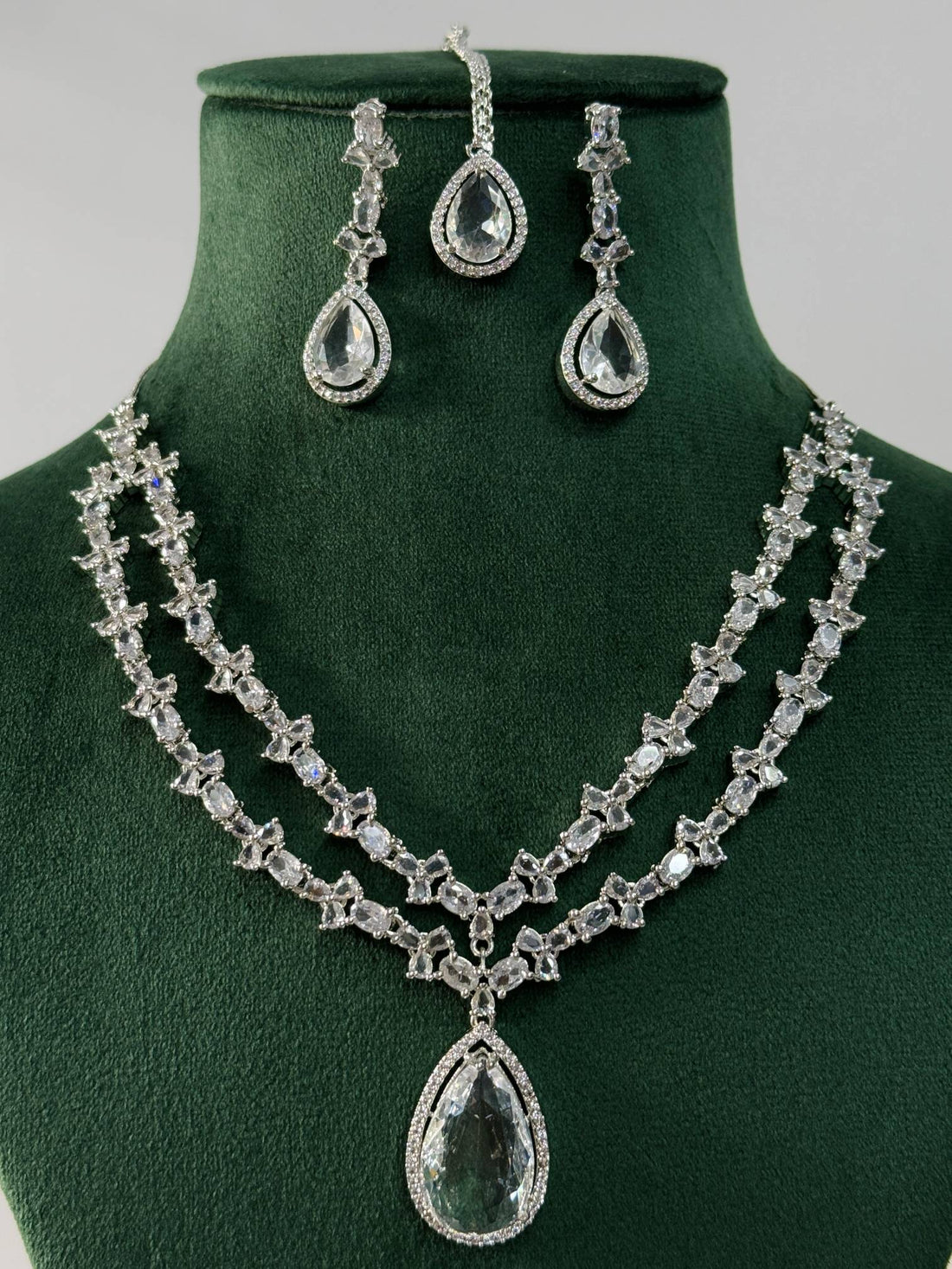 Silver Plated American Diamond Necklace Set with teardrop pendant and matching earrings on green display