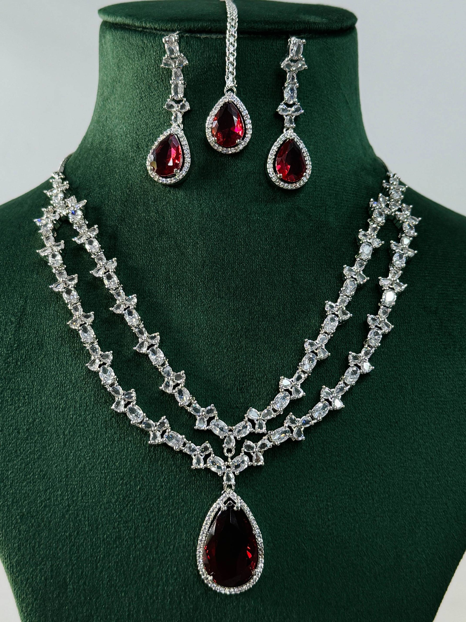 Silver Plated American Diamond Necklace Set with red teardrop stones and matching earrings on green display