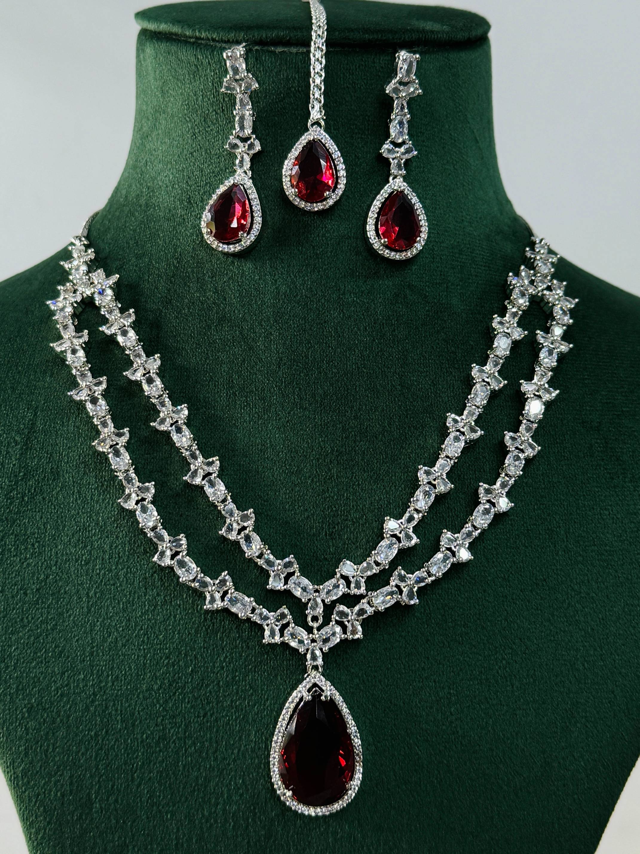 Silver Plated American Diamond Necklace Set with red teardrop stones and matching earrings on green display