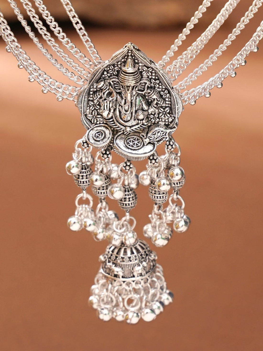 Silver plated saree juda pin with temple deity motifs and jhumka tassels displayed on red silk saree