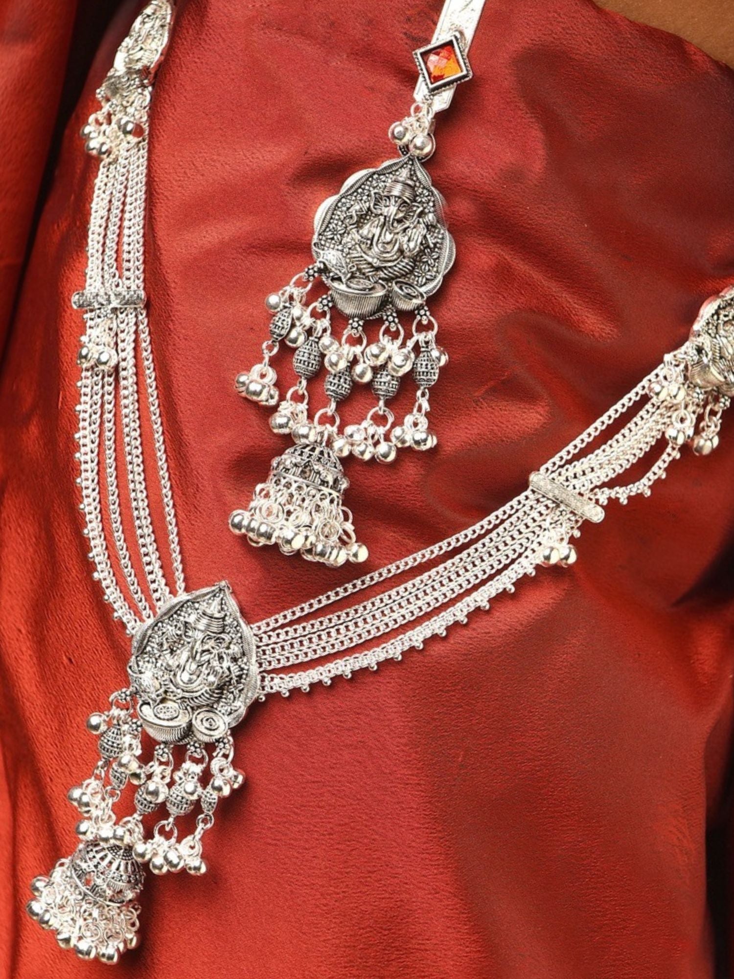 Silver plated saree juda pin with temple deity motifs and jhumka tassels displayed on red silk saree