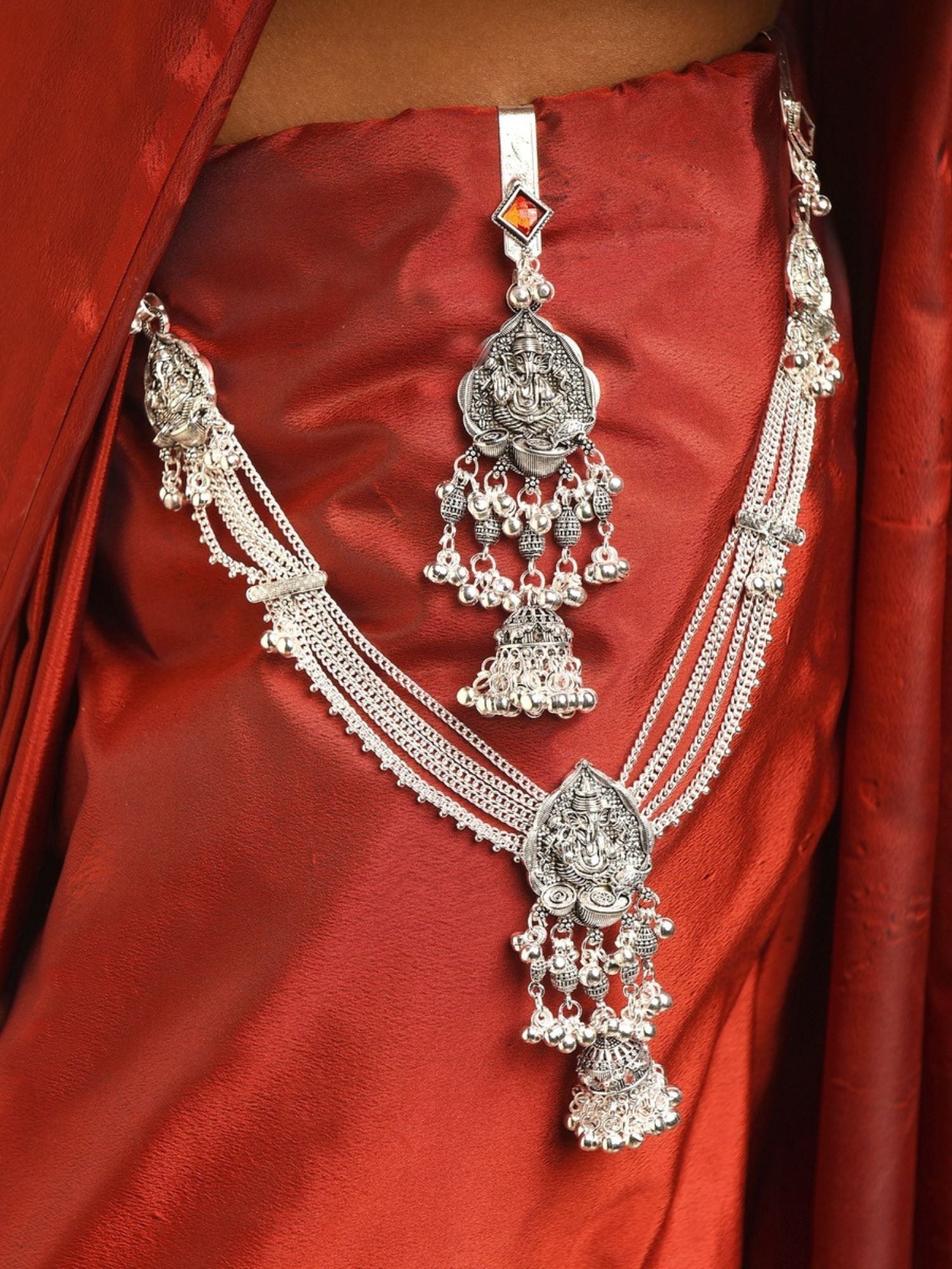 silver plated saree juda pin with intricate jhumka danglers and layered chains worn on red silk saree