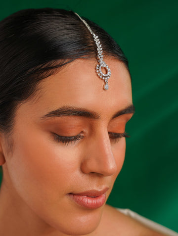 Timeless Silver Plated American Diamond Maangtikka worn on forehead by woman with green background