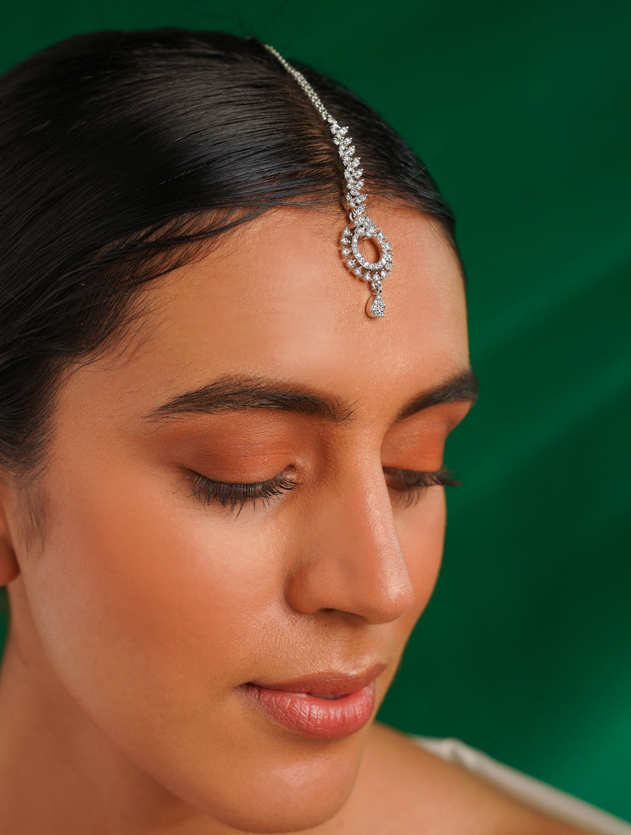 Timeless Silver Plated American Diamond Maangtikka worn on forehead by woman with green background