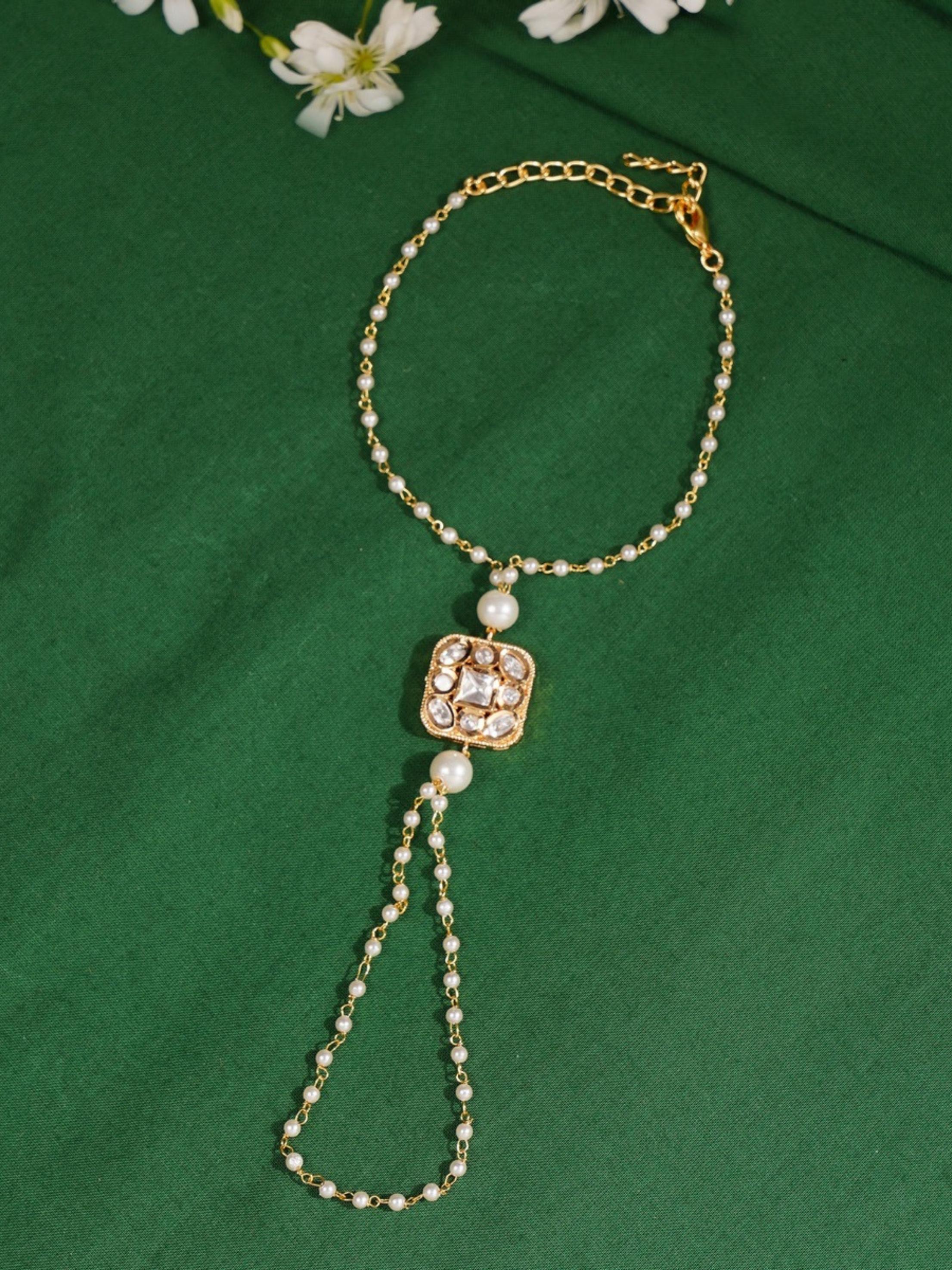 Gold Plated Polki Hand Bracelet by Abdesignsjewellery with pearl and stone detailing on green background