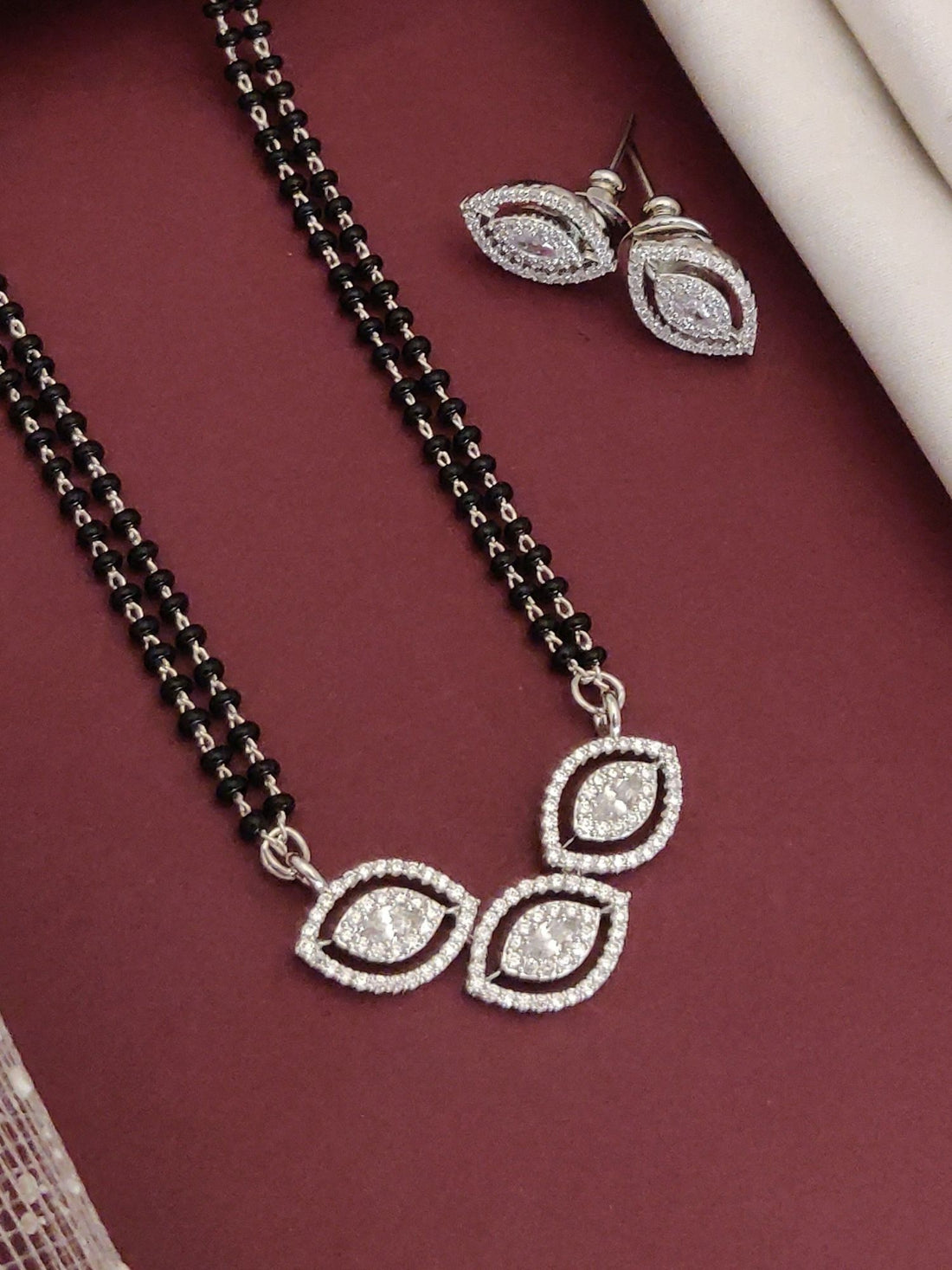 Elegant affordable mangalsutra set with silver accents and matching earrings on a maroon background
