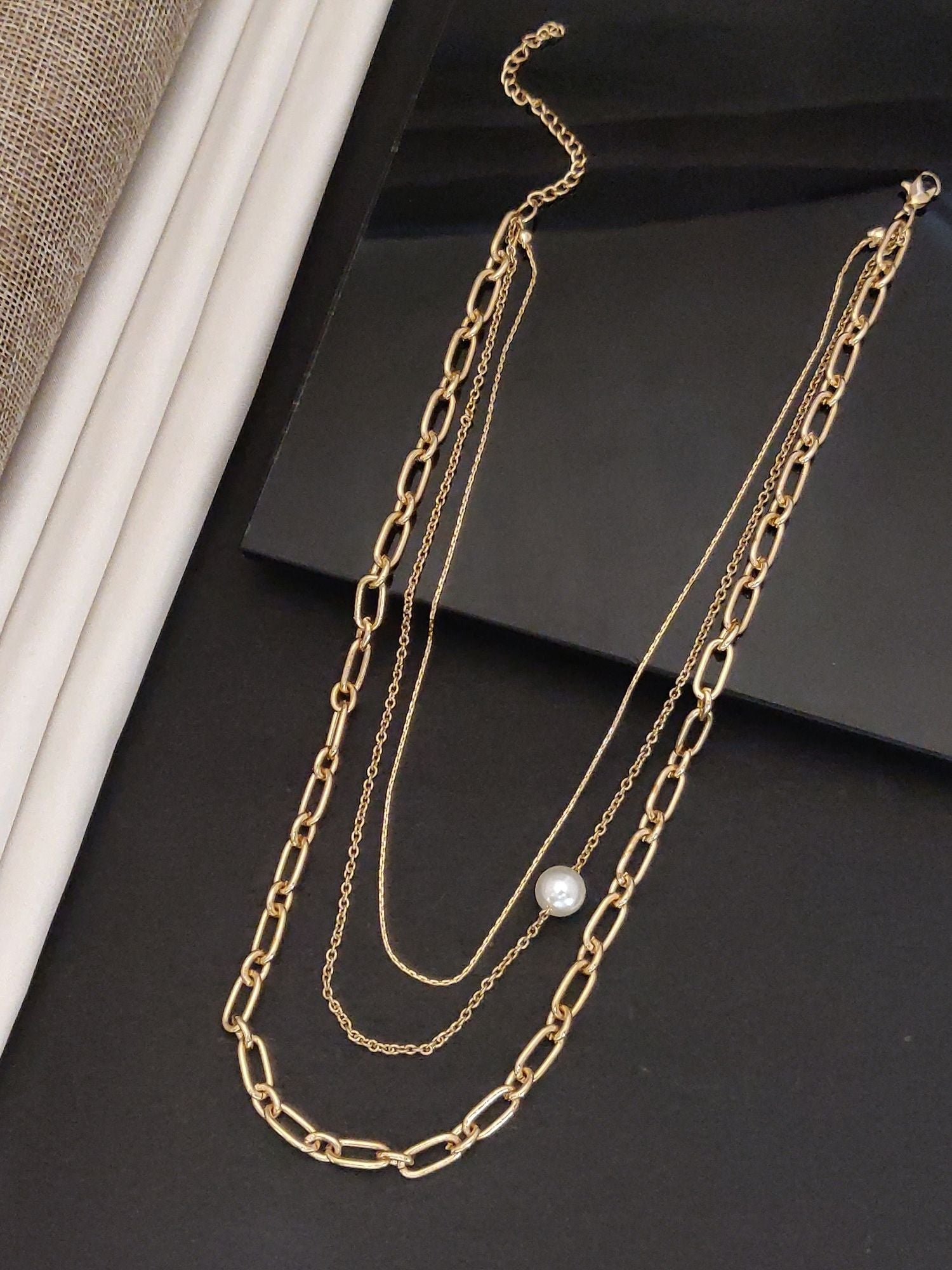 Gold plated layered necklace featuring three delicate chains and a pearl accent for elegant style
