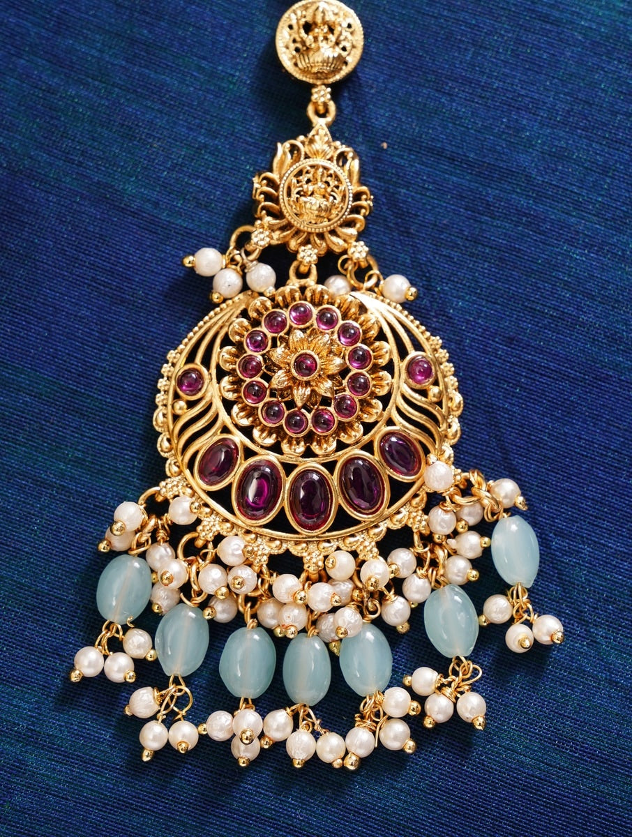 Golden Plated KempStone Studed Maangtikka with purple stones white pearls and light blue beads on dark blue background